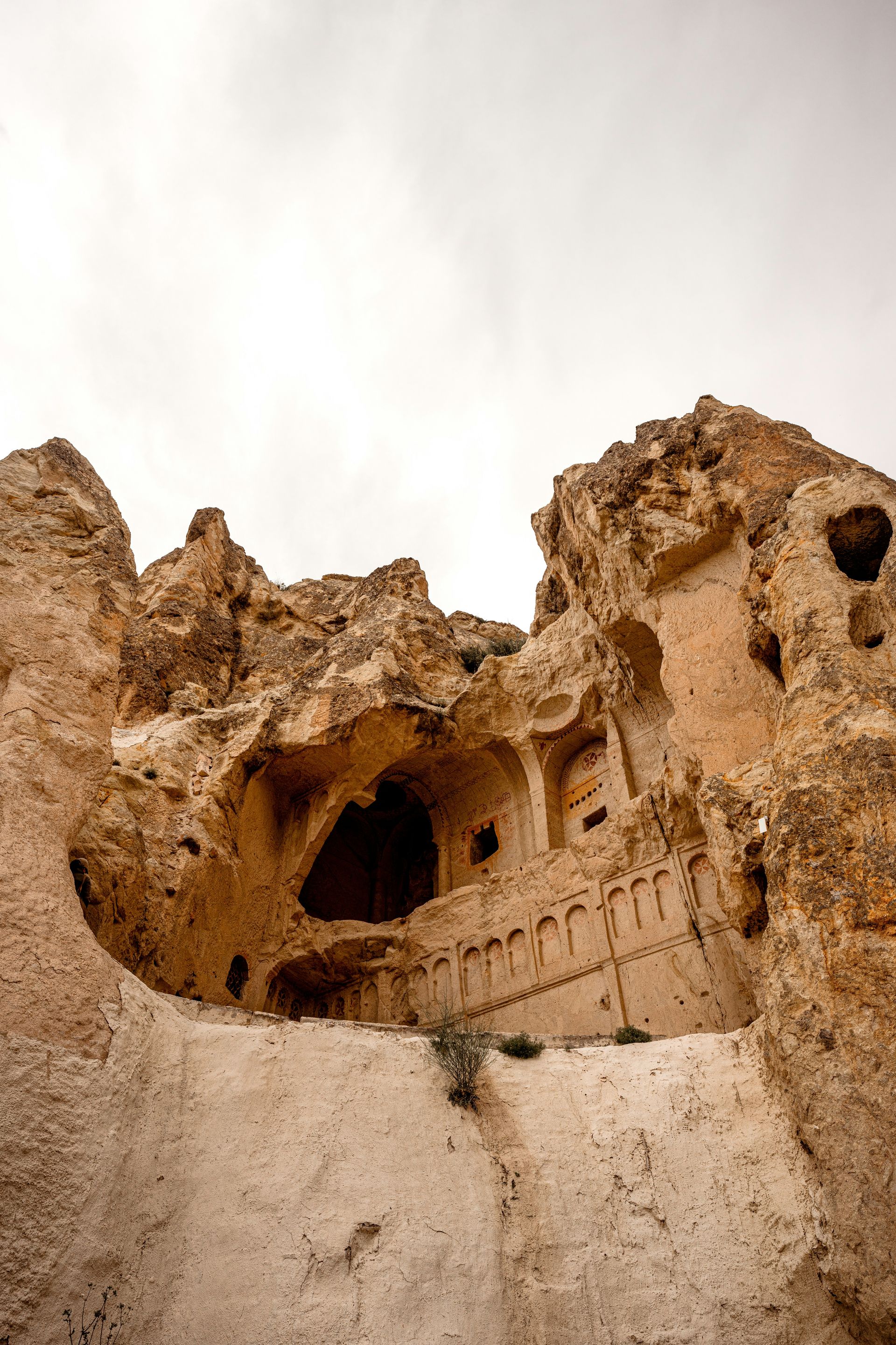 Cave dwellings carved into a light-colored rock formation, with doorways and windows, in Cappadocia, Turkey.