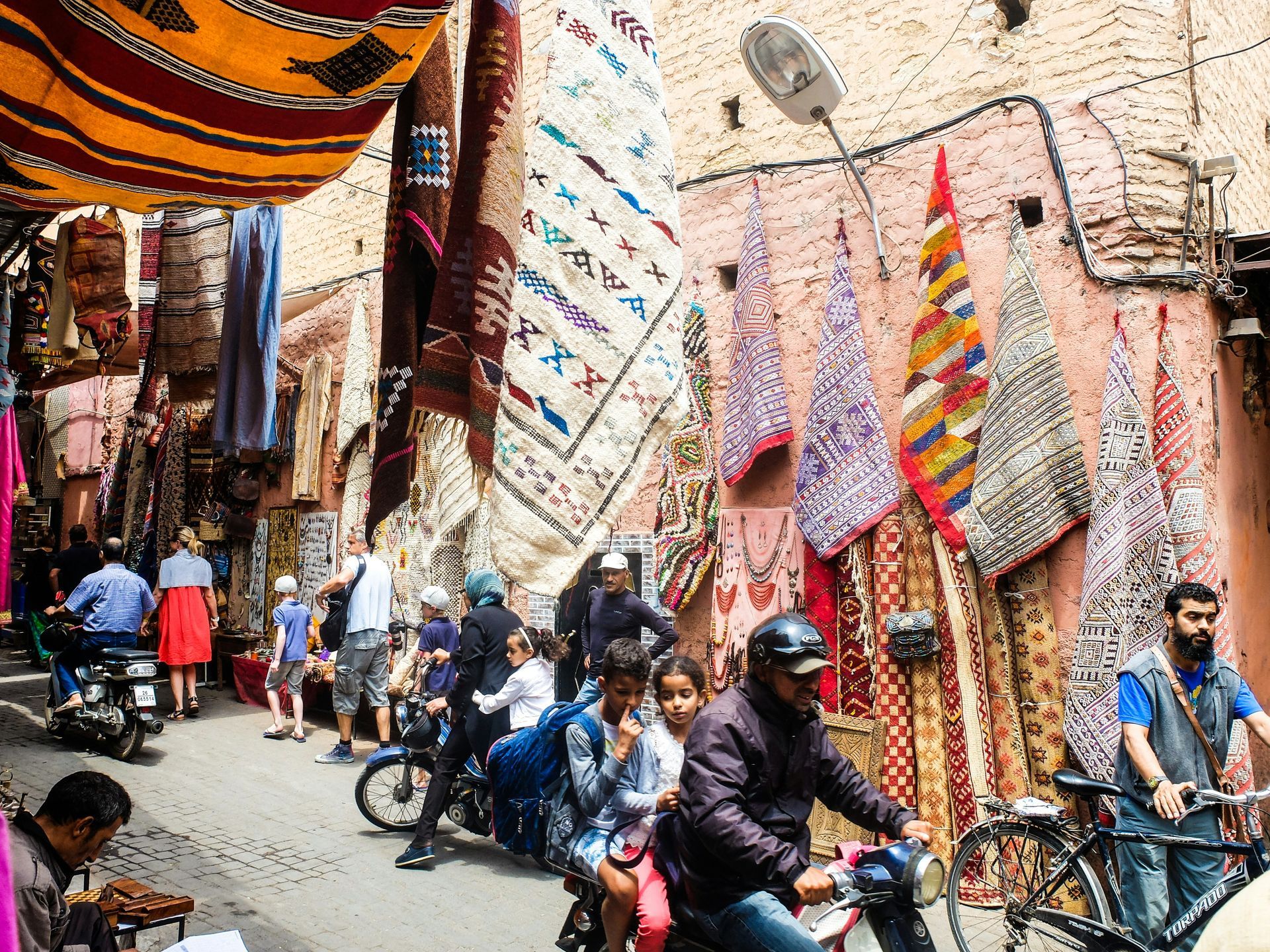 A group of people are riding motorcycles down a narrow street in Marrakesh, Morocco.