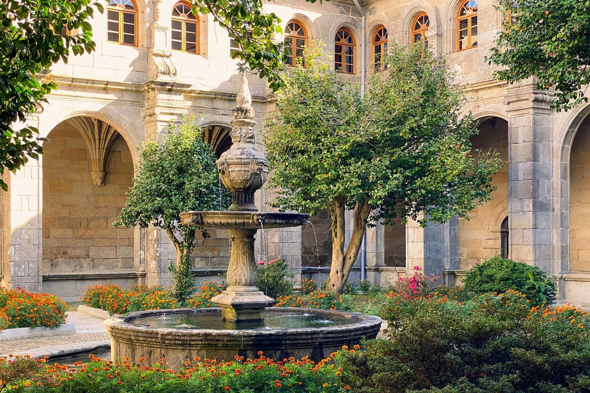 Stone courtyard with fountain, trees, and arched walkways in Santiago de Compostela, Spain.