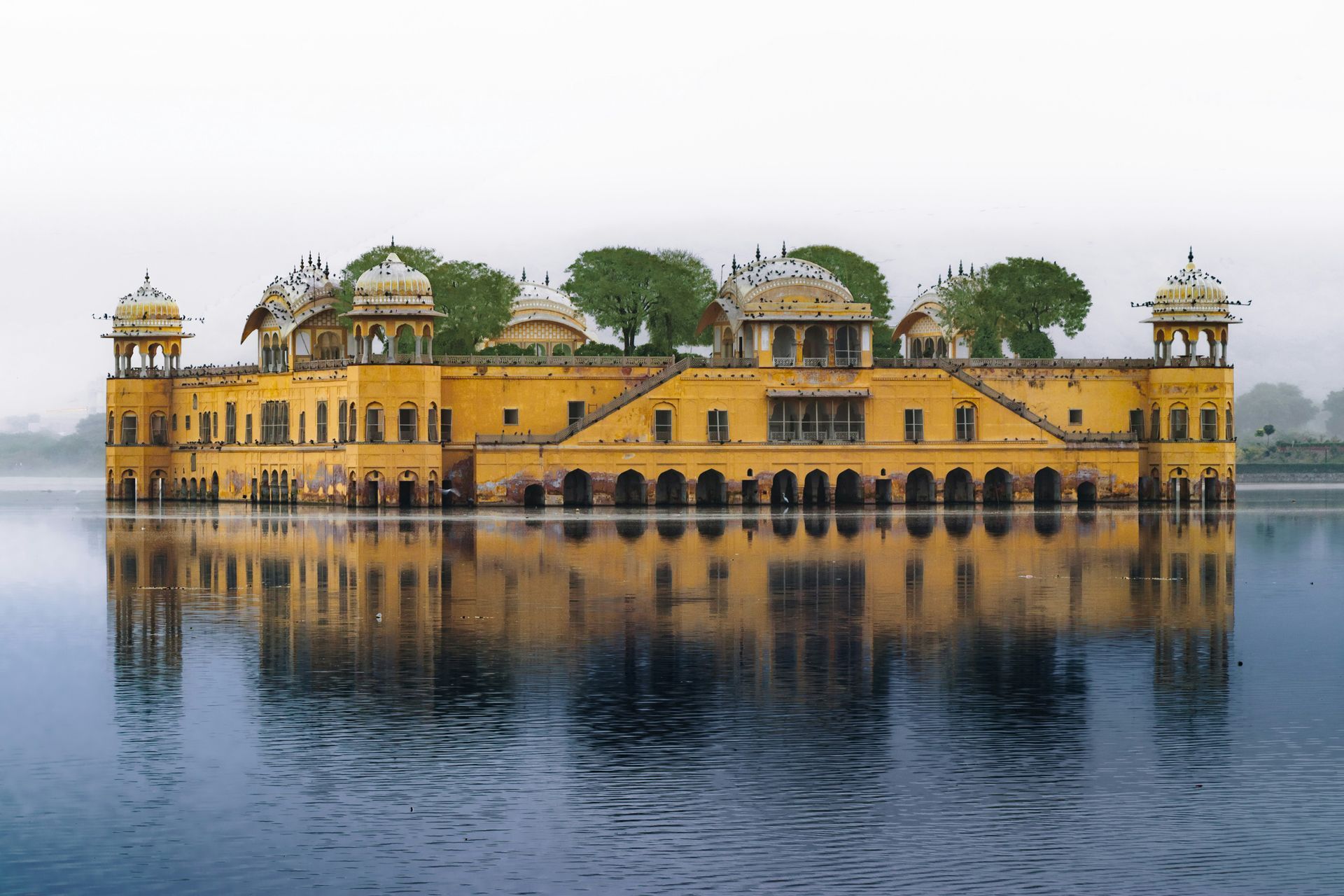 Yellow palace reflecting in blue lake in Jaipur, India.