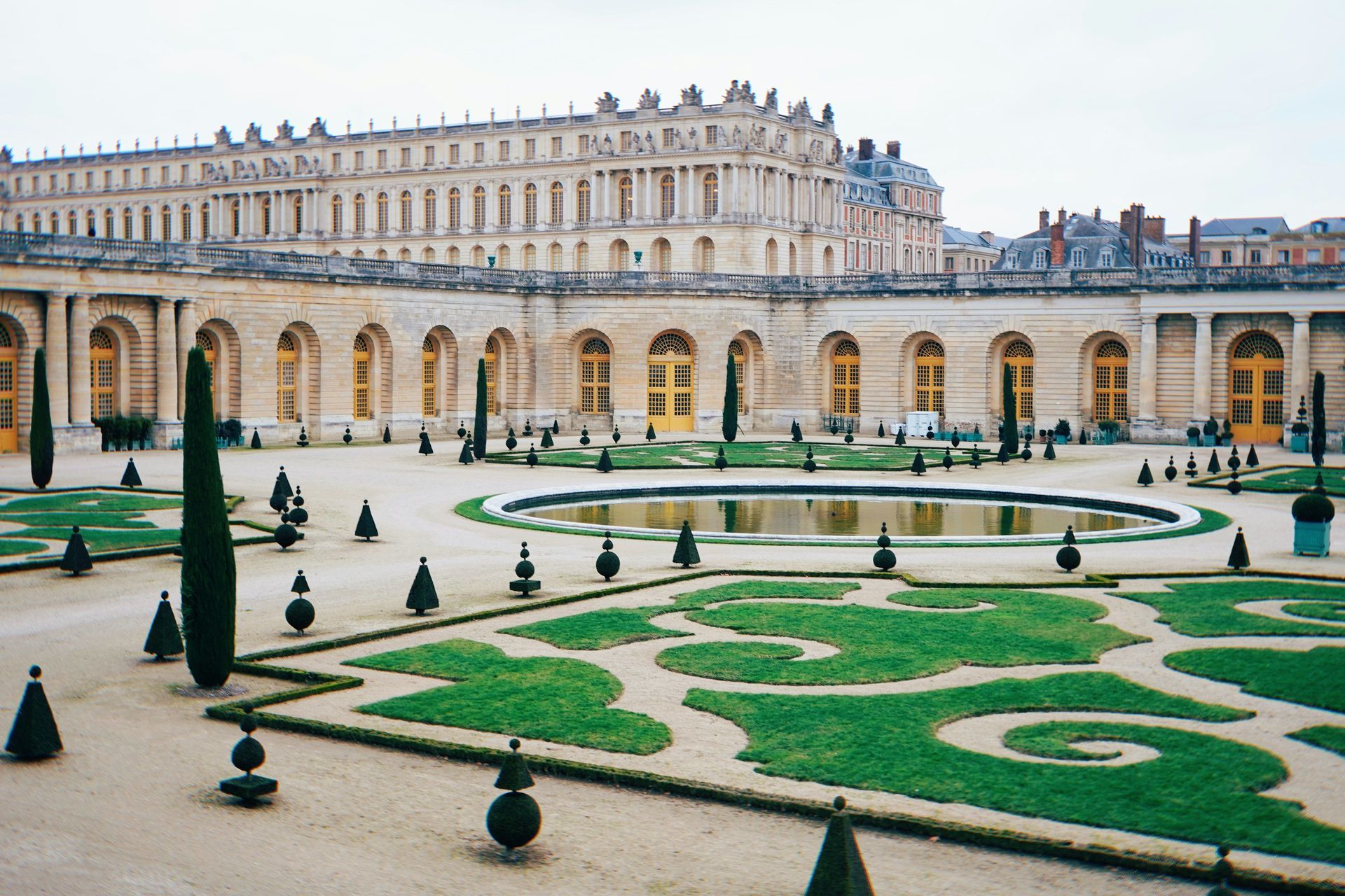 There is a large building in the background and a large garden in the foreground at the Palace of Versailles in France.
