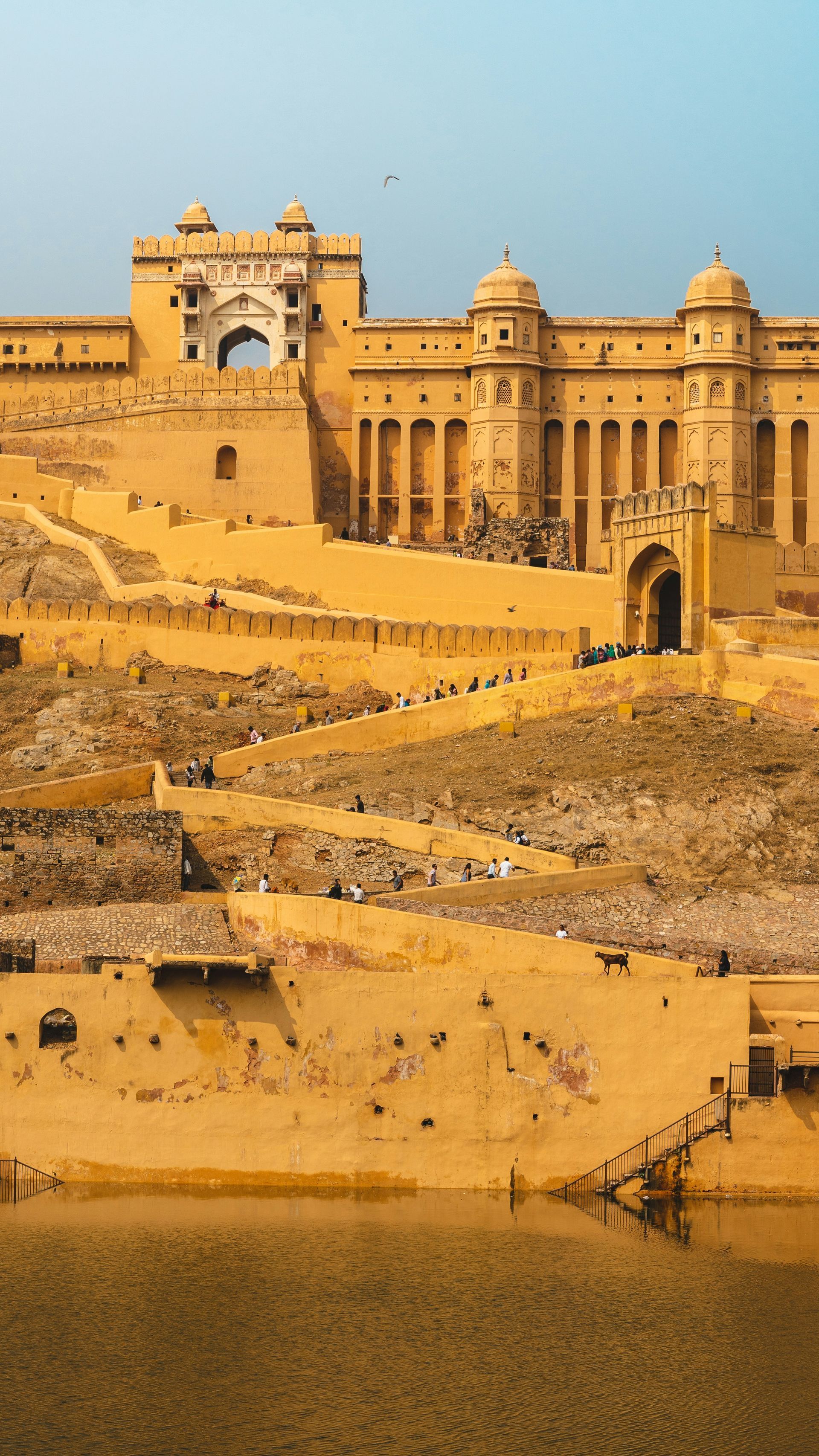 Amber Fort, Jaipur, India, made of sandstone, overlooks a lake, with stairs leading up to arched doorways.