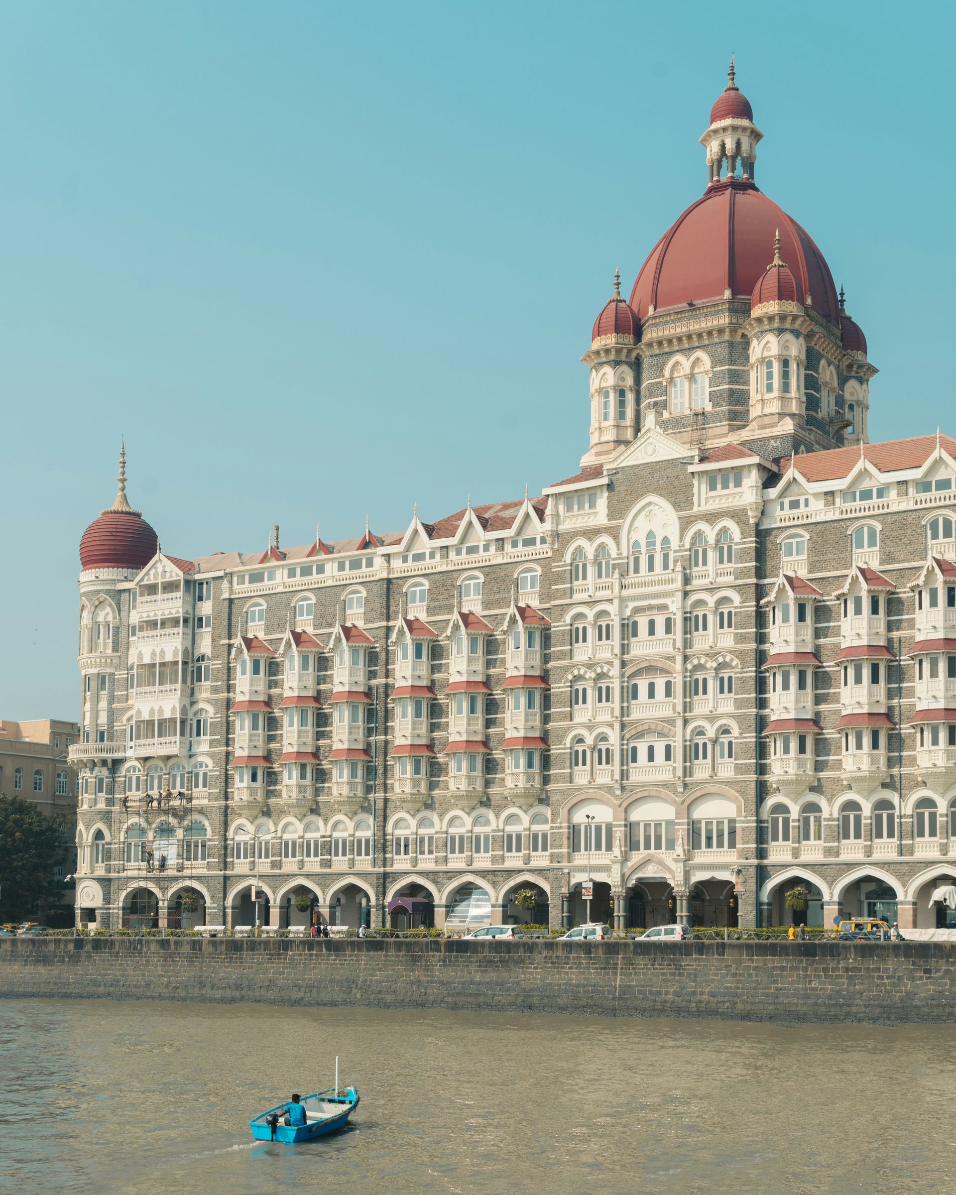 Taj Mahal Palace Hotel, Mumbai, India. Ornate beige and white building with red domes; small boat in the water.