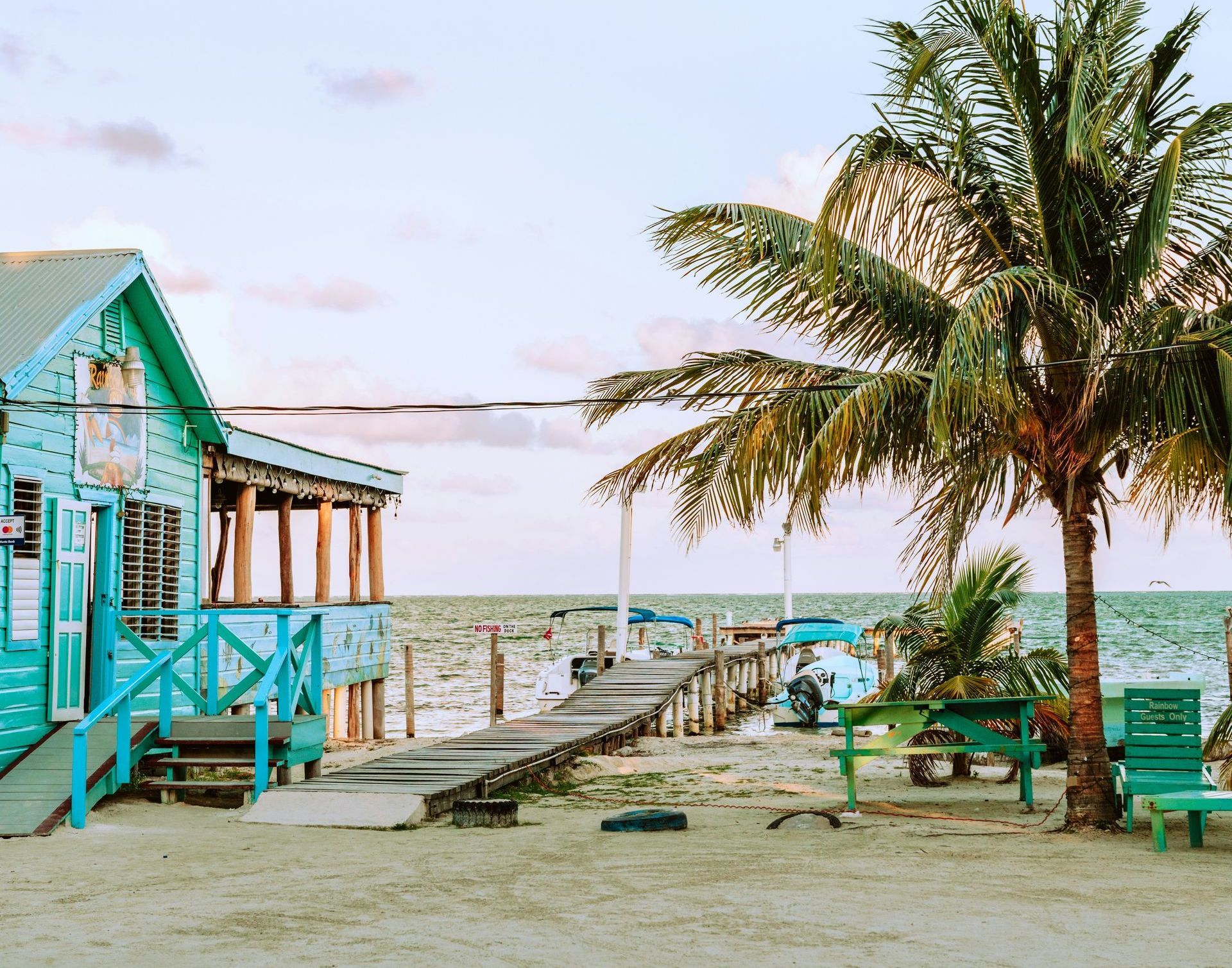 A blue house on a beach with palm trees and a dock in Belize.
