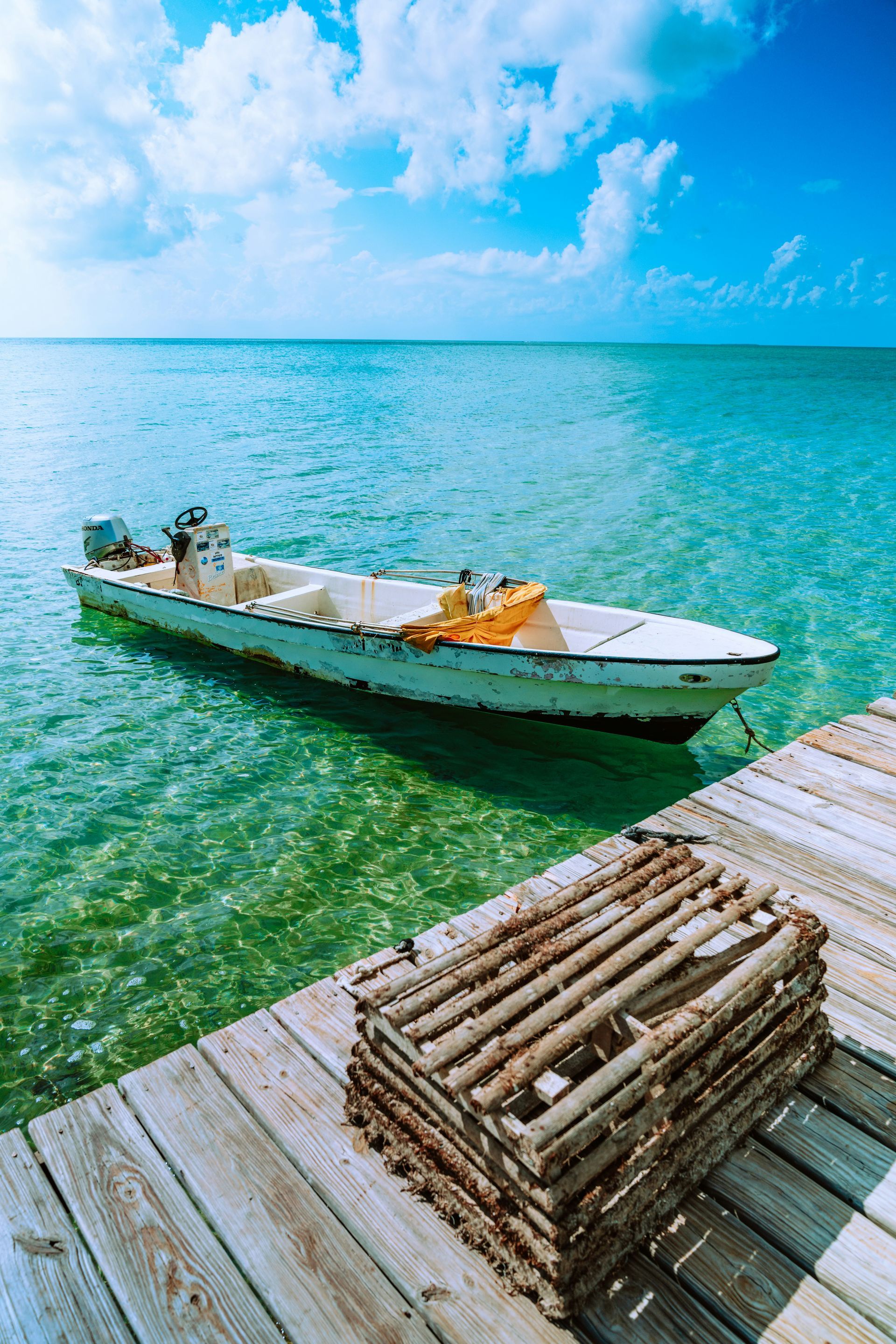 Boat floats in turquoise water near a wooden dock; lobster traps rest on the dock, blue sky overhead in Ambergris Caye, Belize.