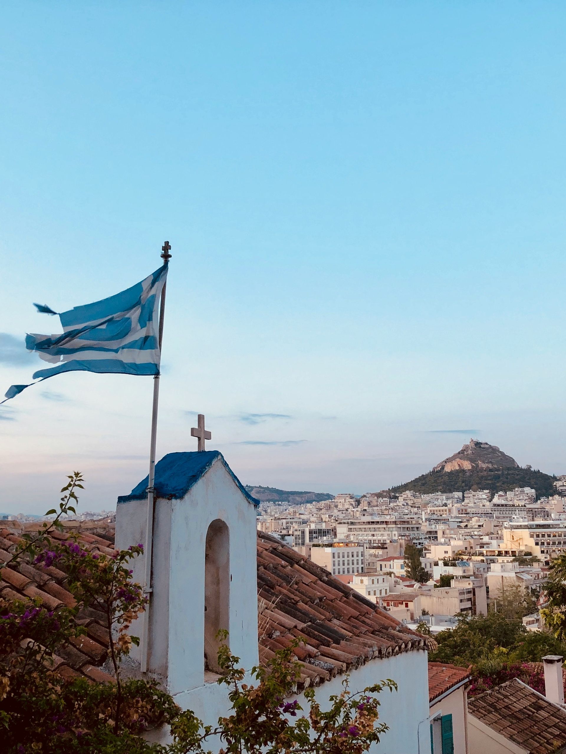A small church with a flag on top of it with Athens, Greece in the background.