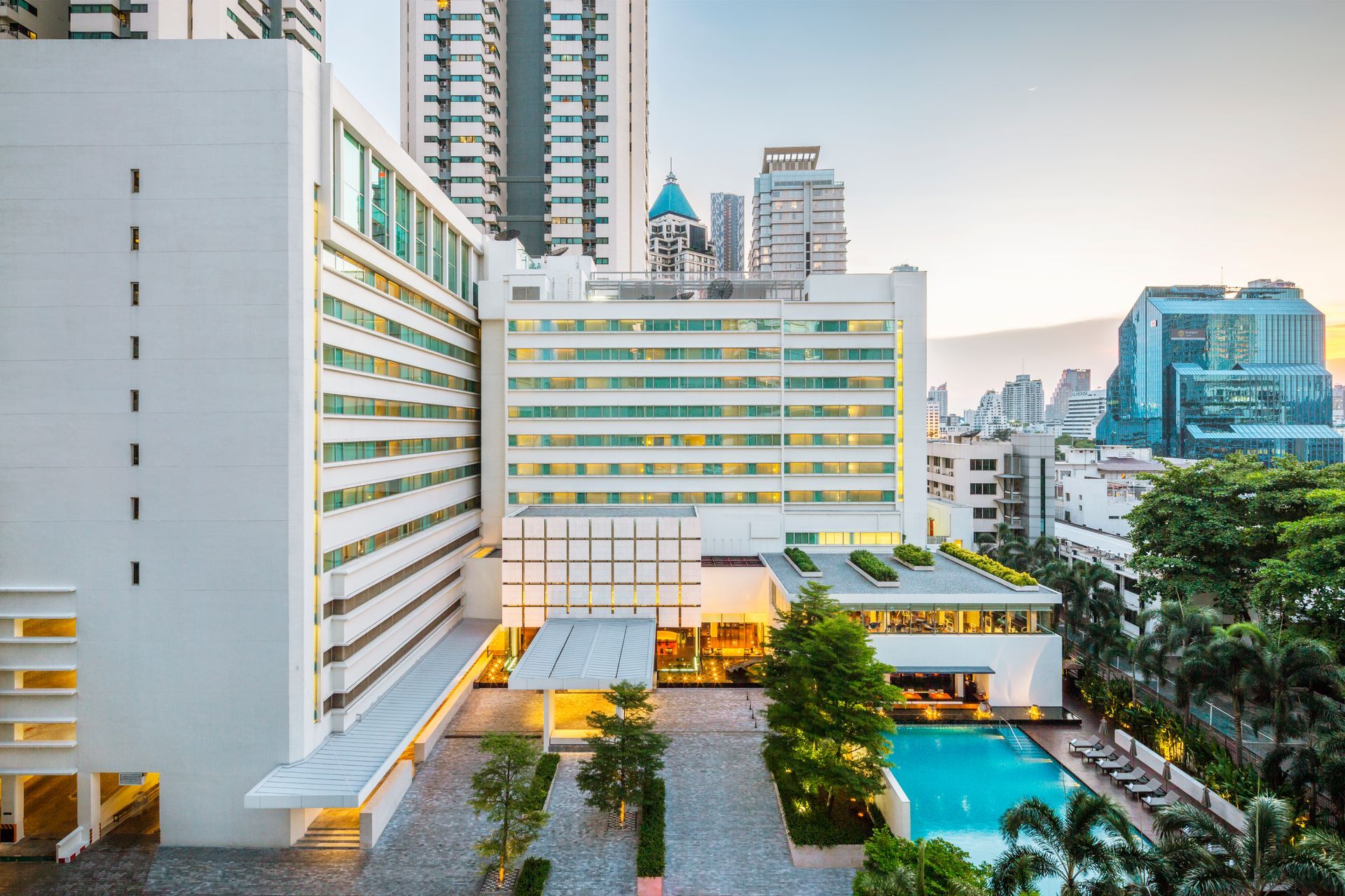 A large white building with a swimming pool in front of it in Bangkok Thailand at Como Hotel. 