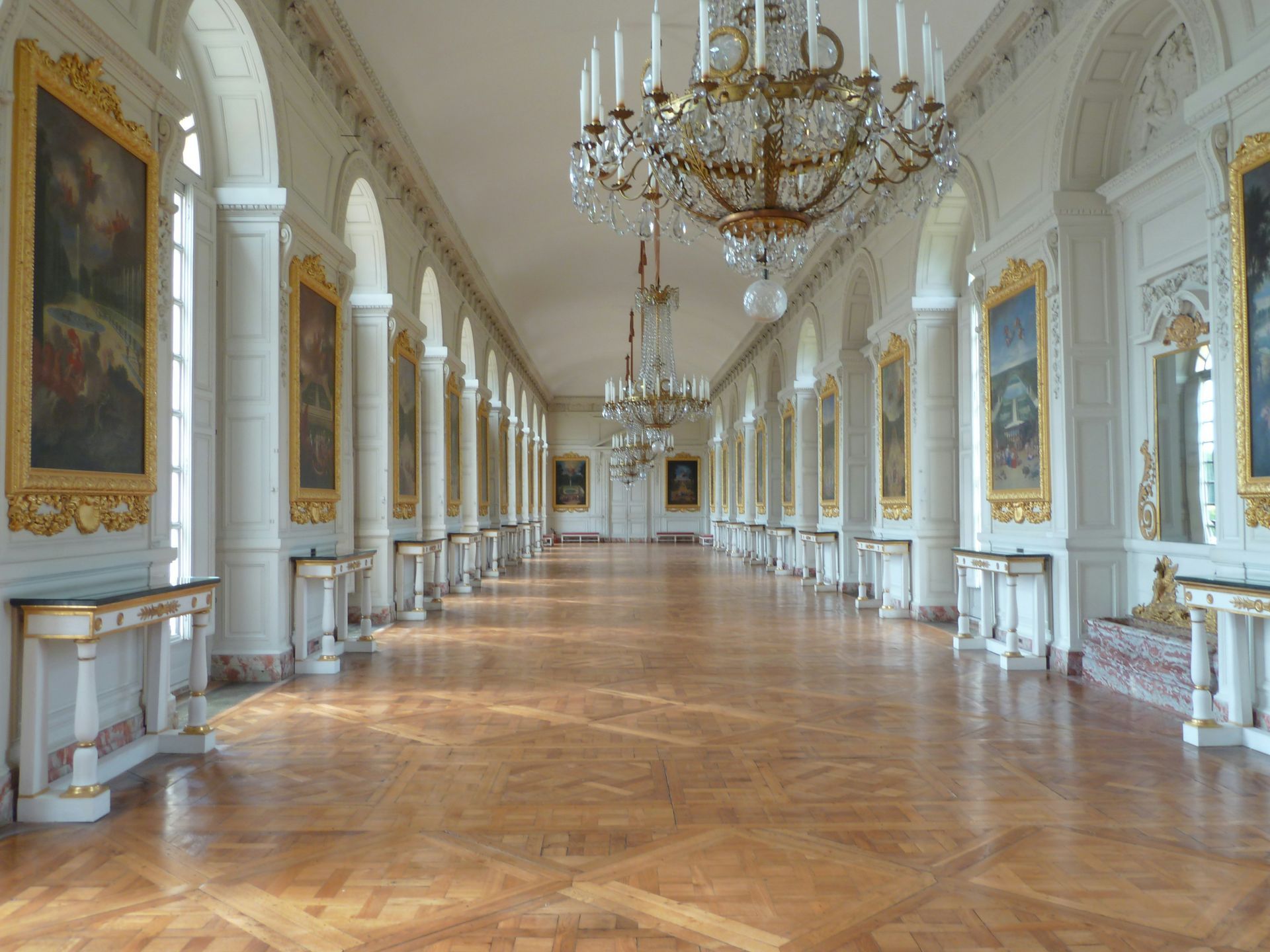 A long hallway with columns and a chandelier hanging from the ceiling at the Palace of Versailles in France.