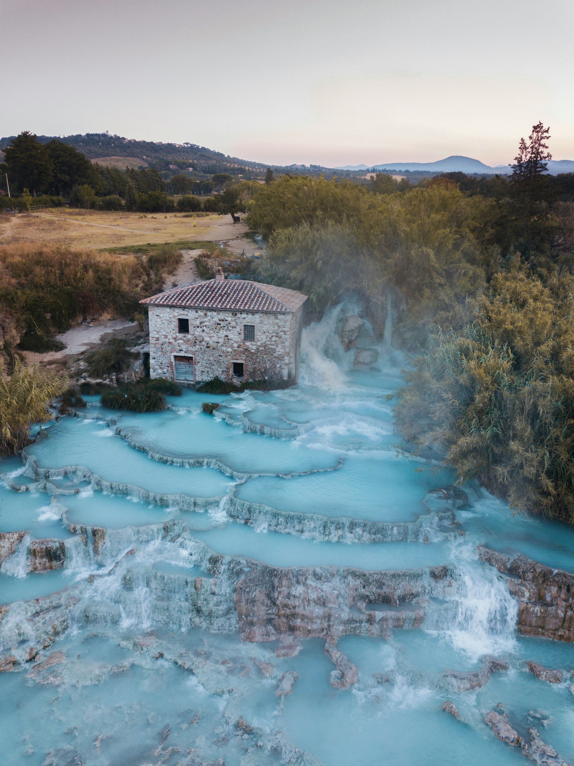 An aerial view of the hot spring Cascate del Mulino with a house in the background in Tuscany, Italy.