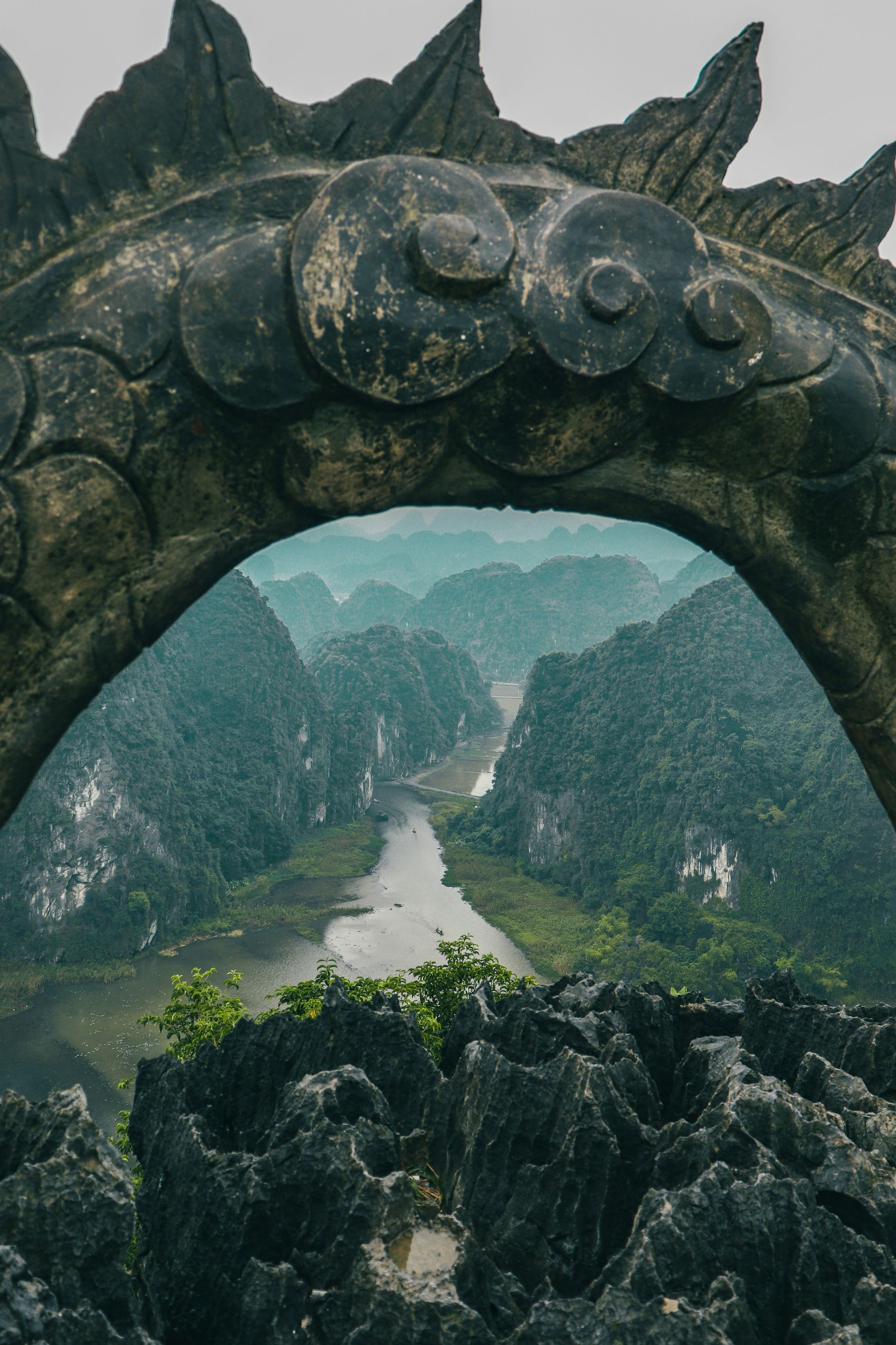 Stone arch framing a river winding through lush, misty mountains in Ninh Bình, Vietnam.
