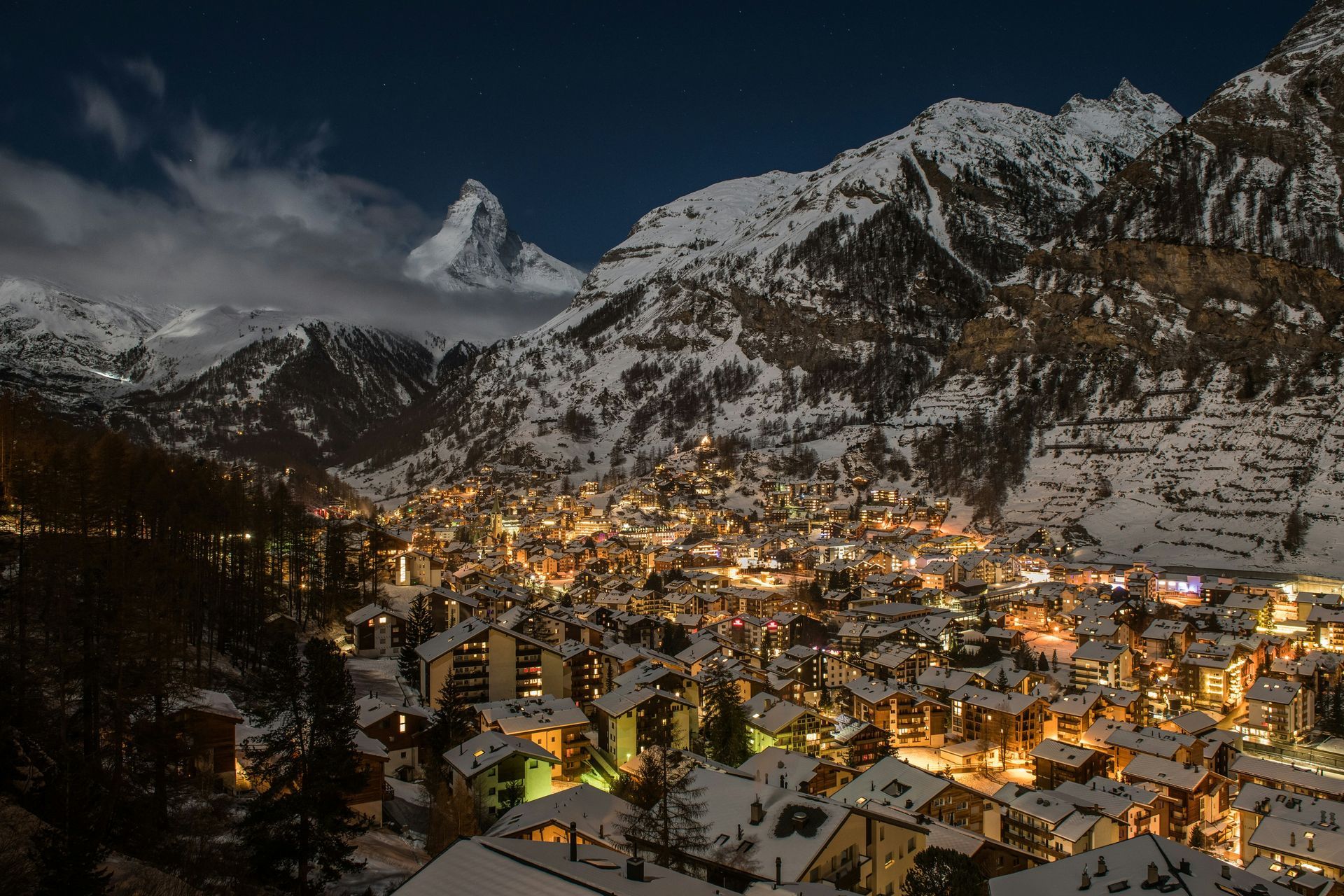 Night view of Zermatt village nestled beneath snowy mountains with the Matterhorn peak.