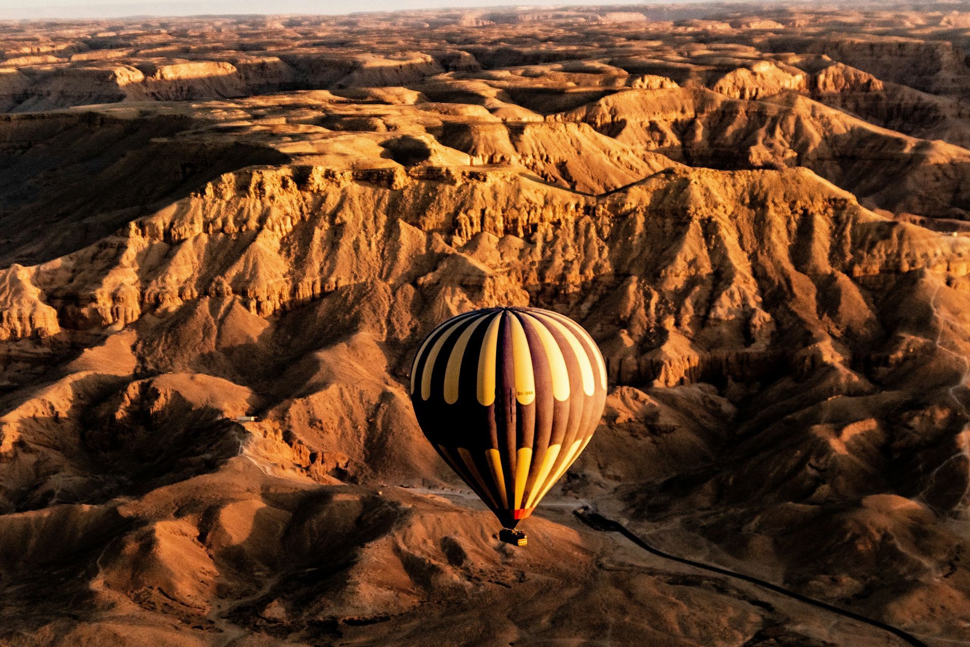 A hot air balloon is flying over a desert landscape in Luxor, Egypt.