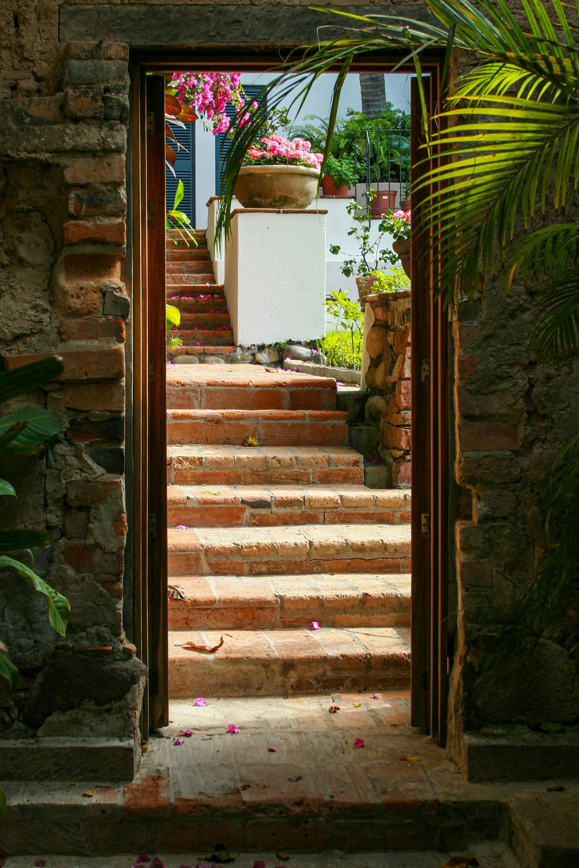 Brick doorway frames a staircase leading upwards. Flowers and greenery surround the stairs in Puerto Vallarta, Mexico.