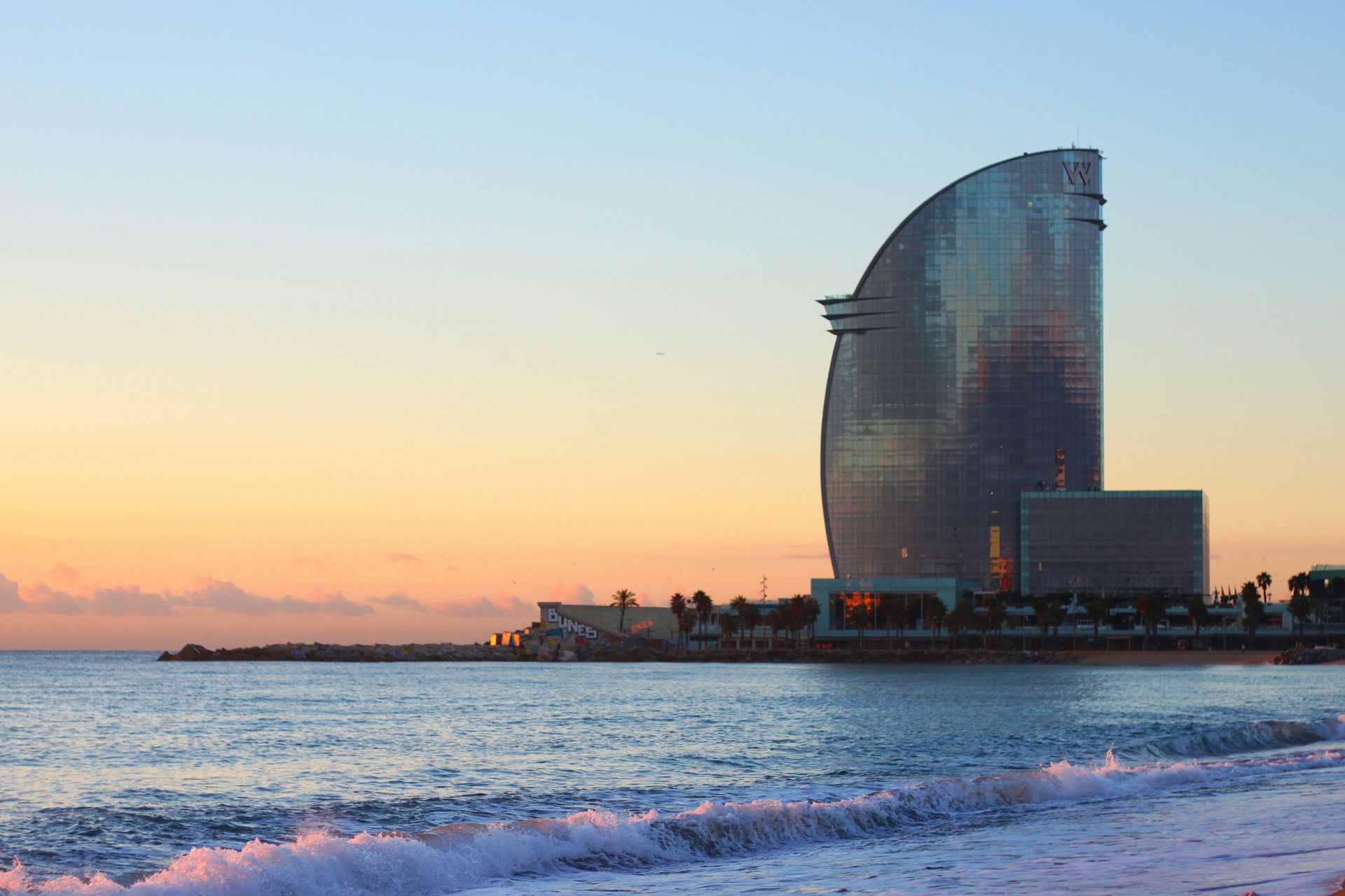 Beachfront hotel at sunrise in Barcelona, Spain. Waves rolling in, building reflects the sky's colors.