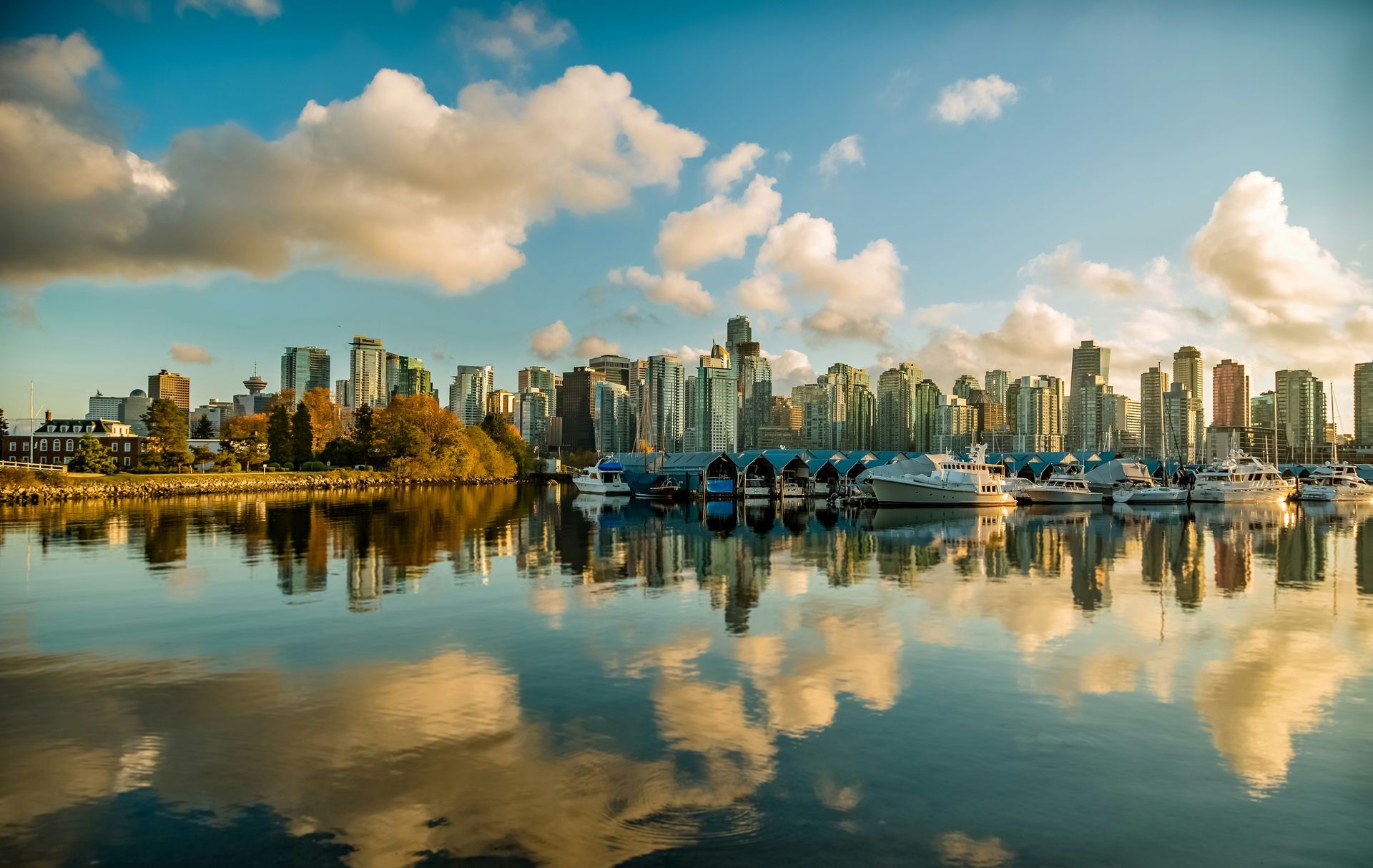 Vancouver skyline reflected in calm water, under a partly cloudy sky. Buildings are mirrored below.