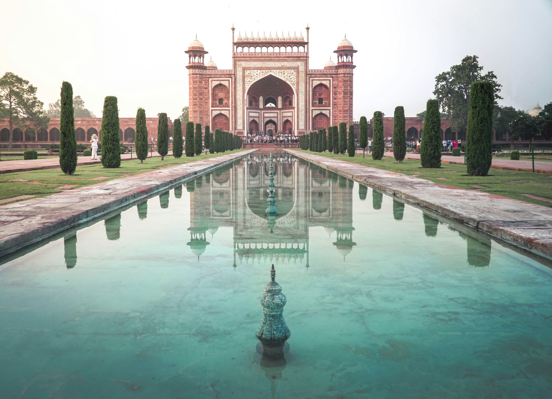 Grand gateway and reflecting pool at the Taj Mahal. Red sandstone, white marble, water, trees.