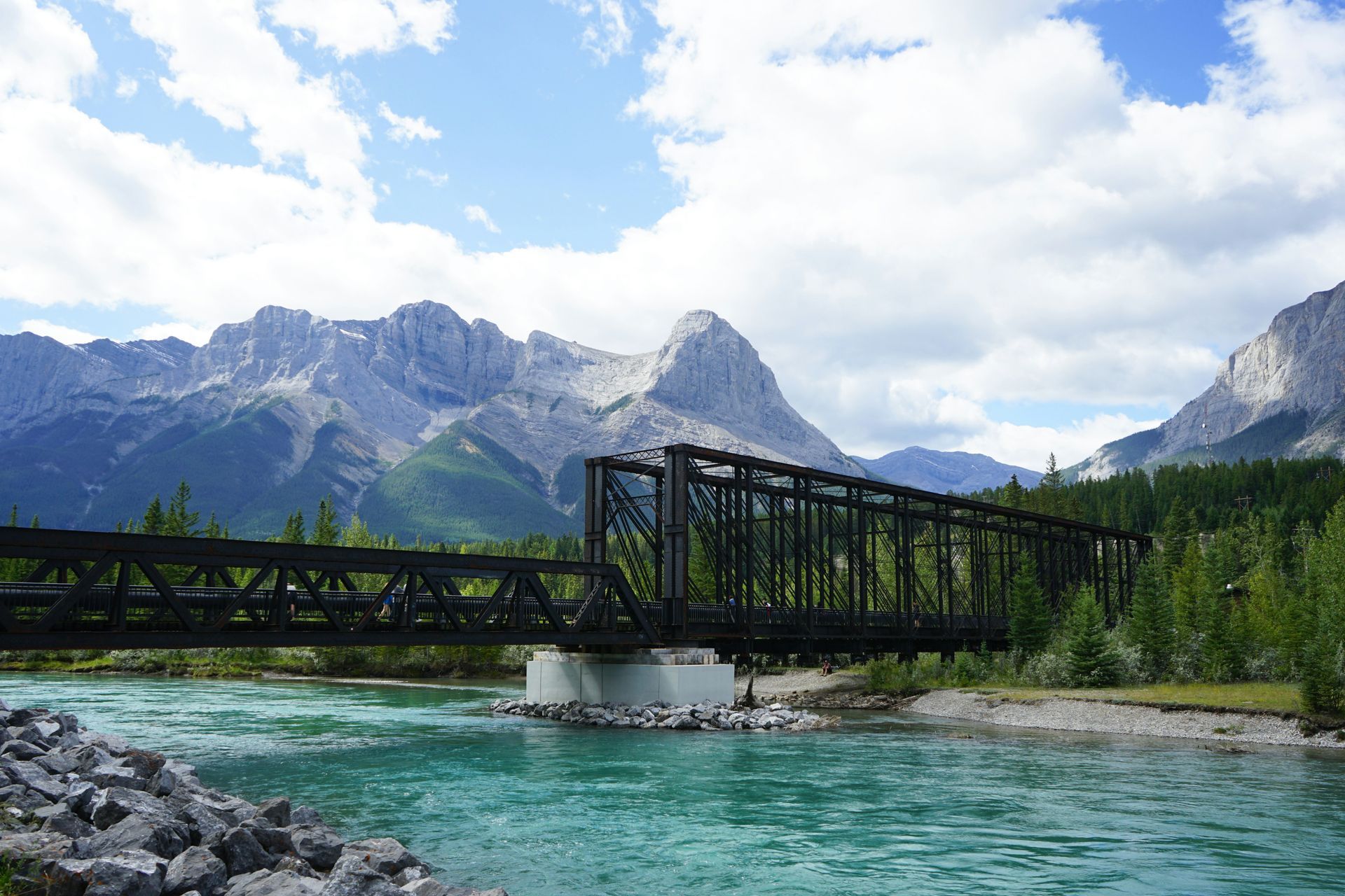 Railway bridge spans a turquoise river, mountains rise in the background in Canmore, Canada.