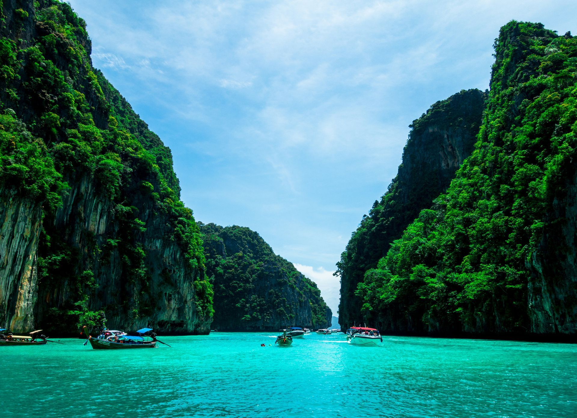 Boats are floating in the water between two mountains in Phuket, Thailand.