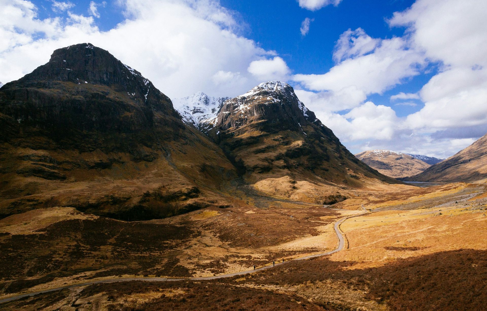 Mountain landscape with brown and tan valley, under cloudy sky. Snow on peaks in Glencoe, Scotland.