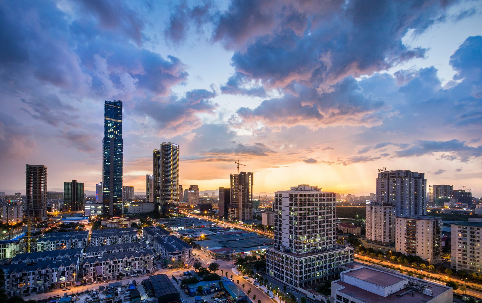 Hanoi, Vietnam skyline at sunset with tall buildings and dramatic clouds.