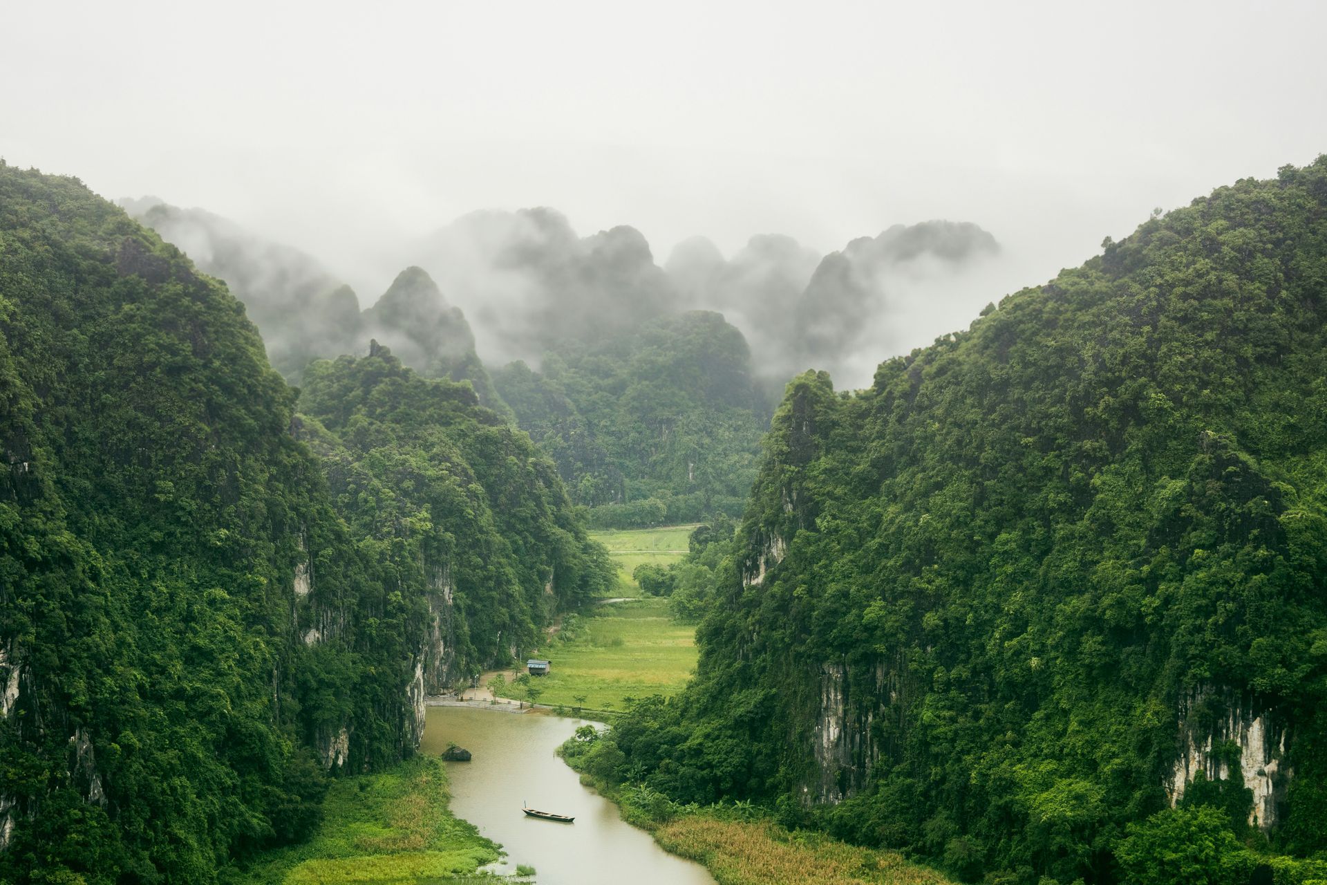 Green mountains and a river under a foggy sky in Ninh Bình, Vietnam.