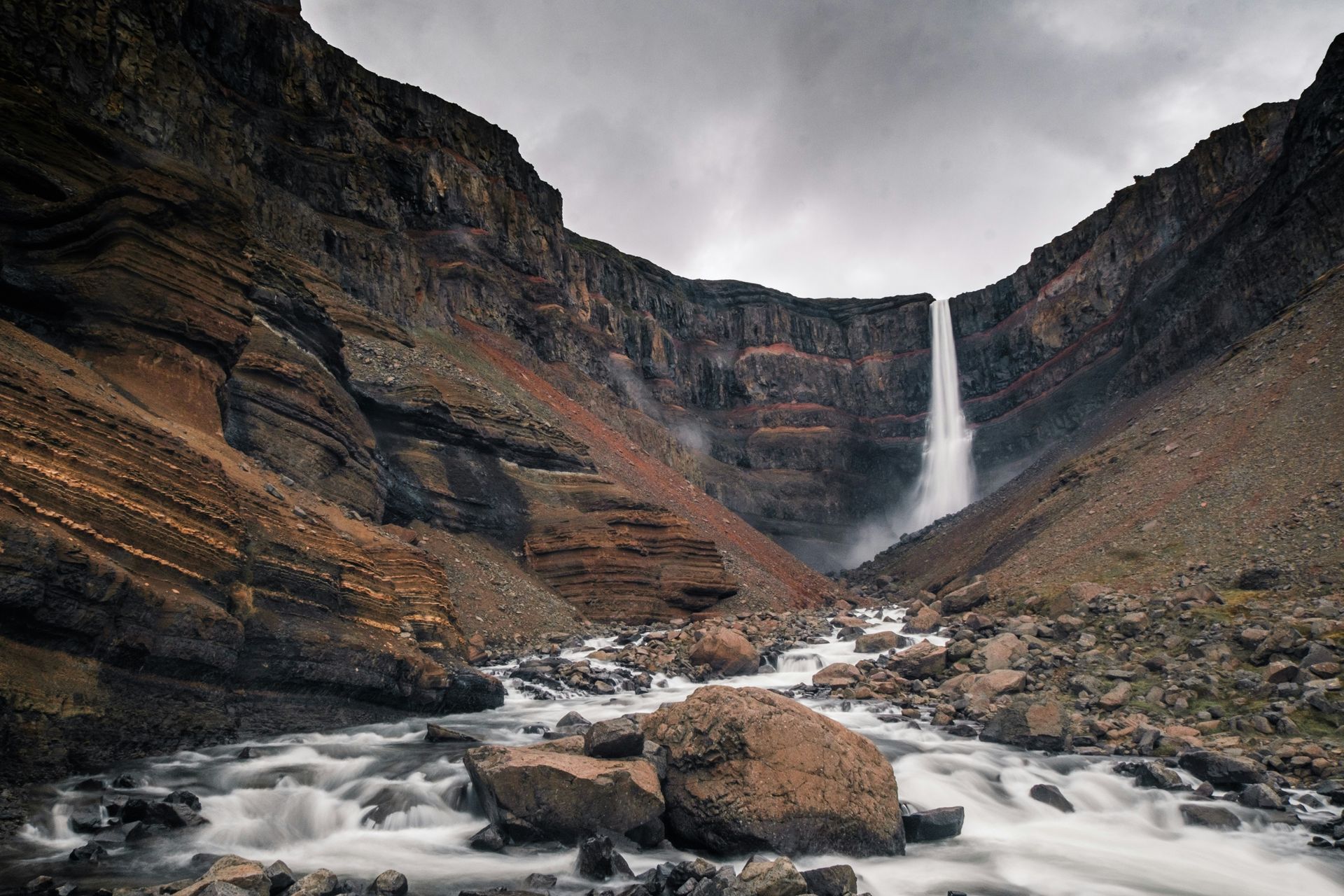 The Hengifoss Waterfall cascading down a canyon with a rocky riverbed in Iceland.