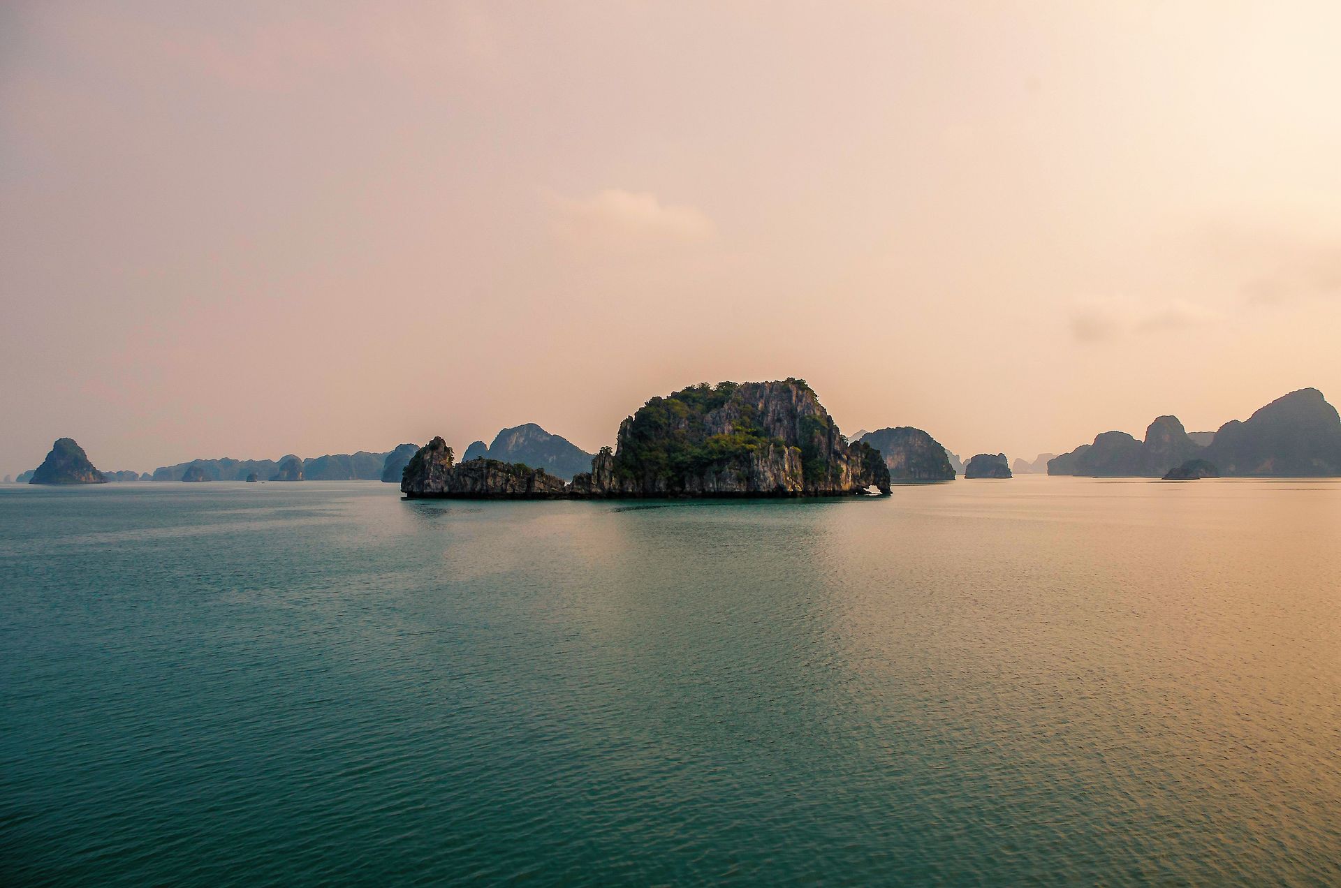 Emerald water with limestone islands under a hazy sky in Halong Bay, Vietnam.