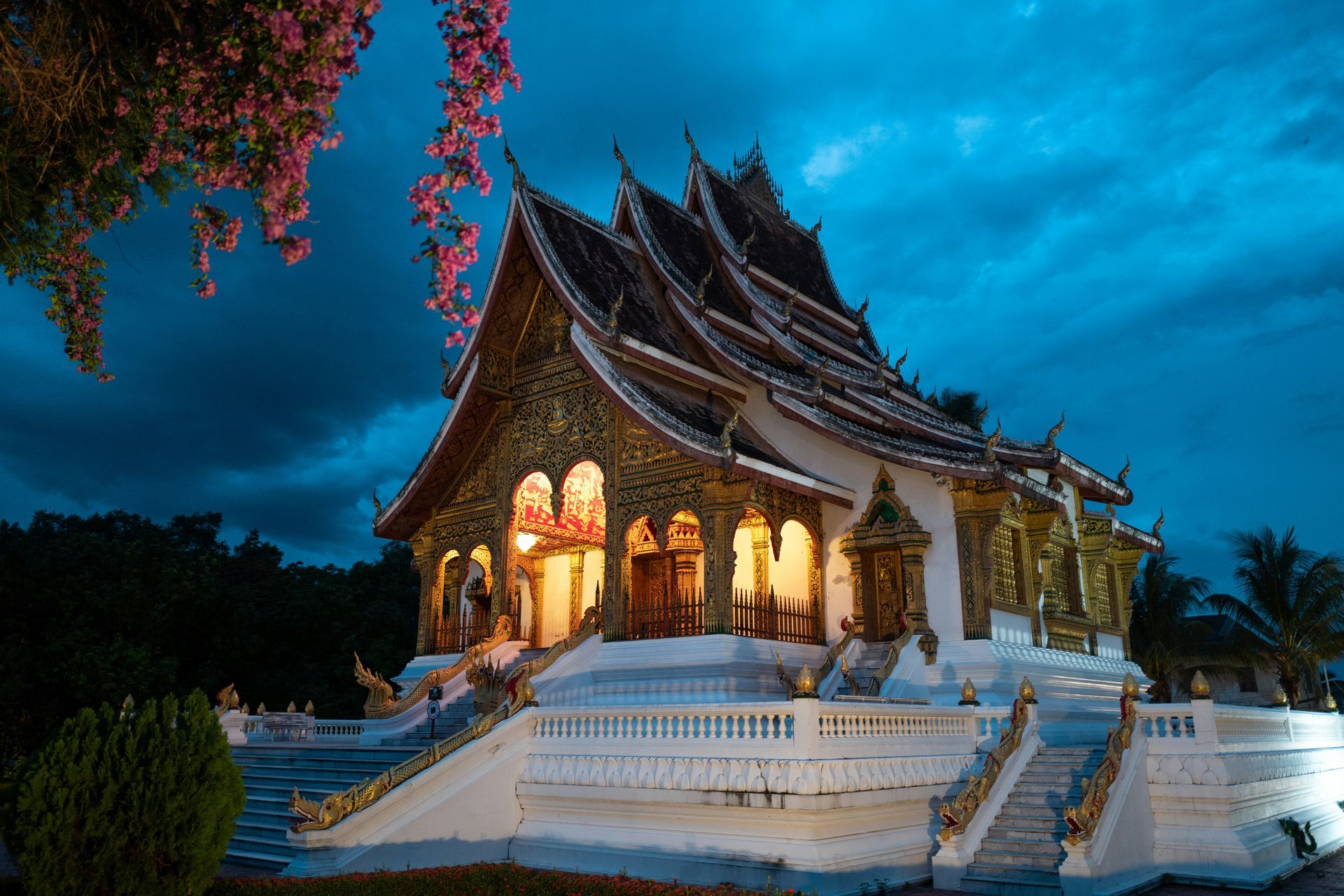Ornate, gold-trimmed temple illuminated at dusk, with a tiered roof and steps in Luang Prabang, Laos.