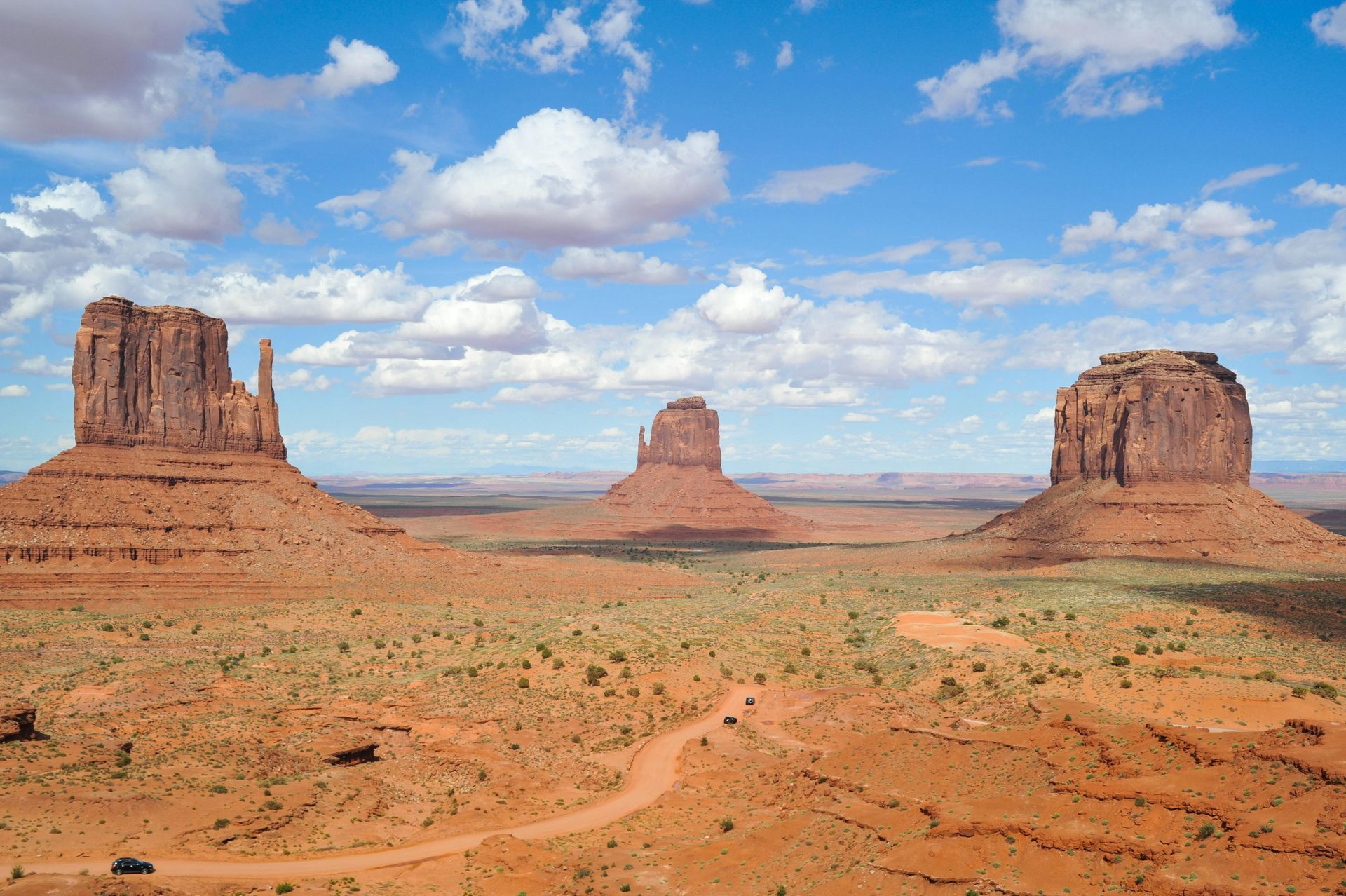 A desert landscape with rock formations and a dirt road in the foreground at Monument Valley in Arizona.