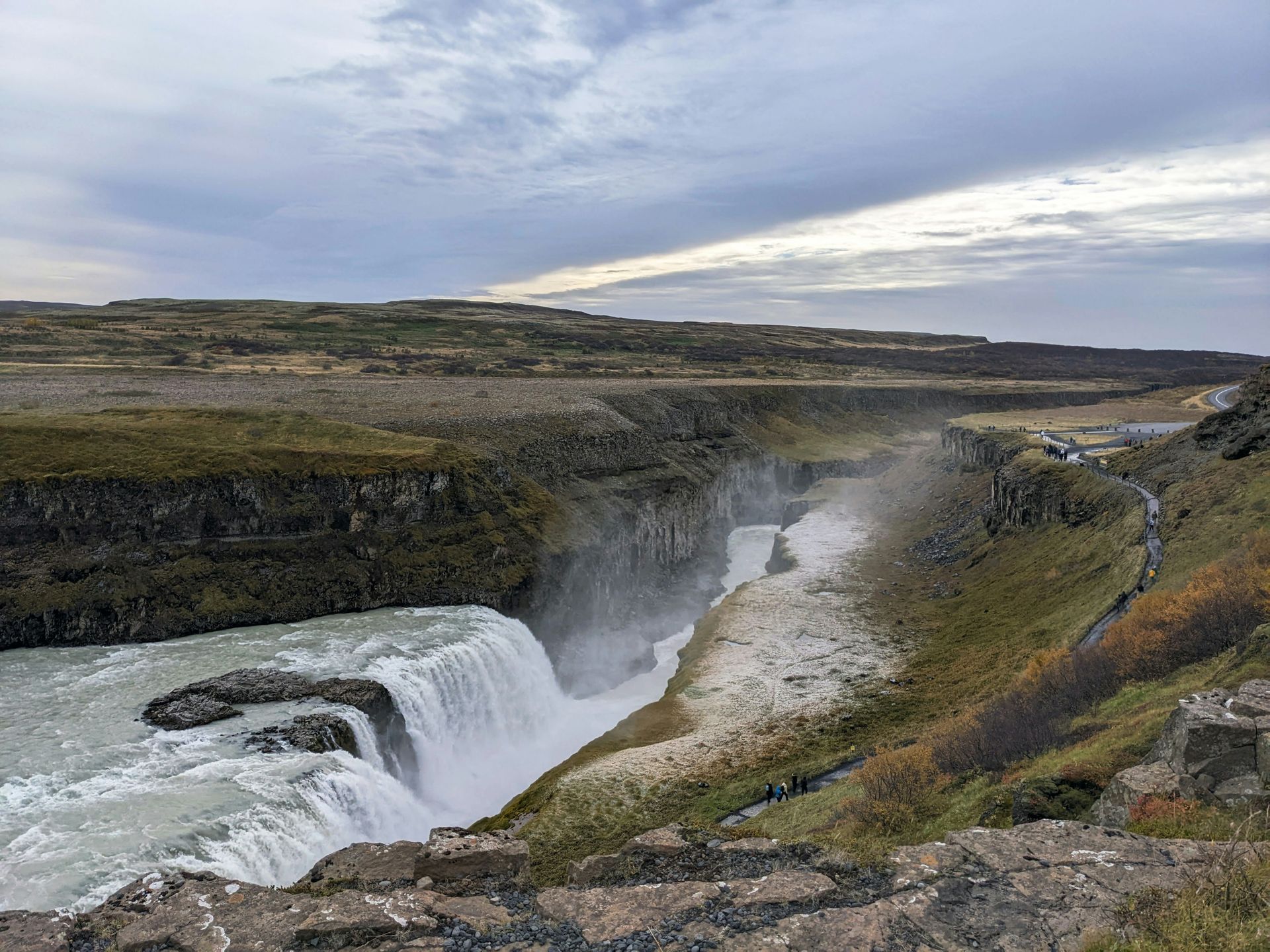 Gullfoss Falls cascading into a canyon under a cloudy sky. Brown and green landscape surrounds in Iceland.