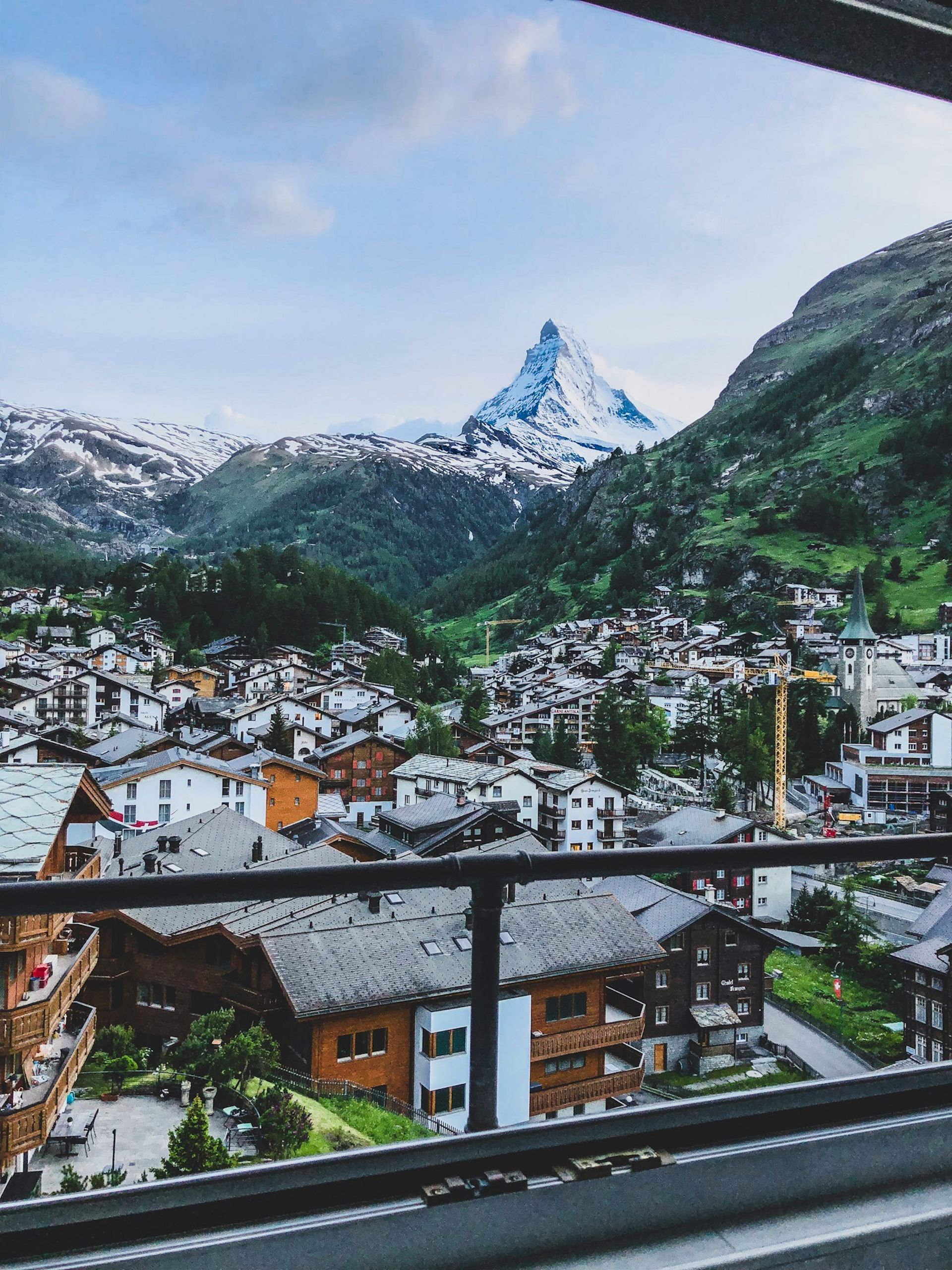Zermatt, Switzerland in a valley below snow-capped mountains. View framed by dark railing.
