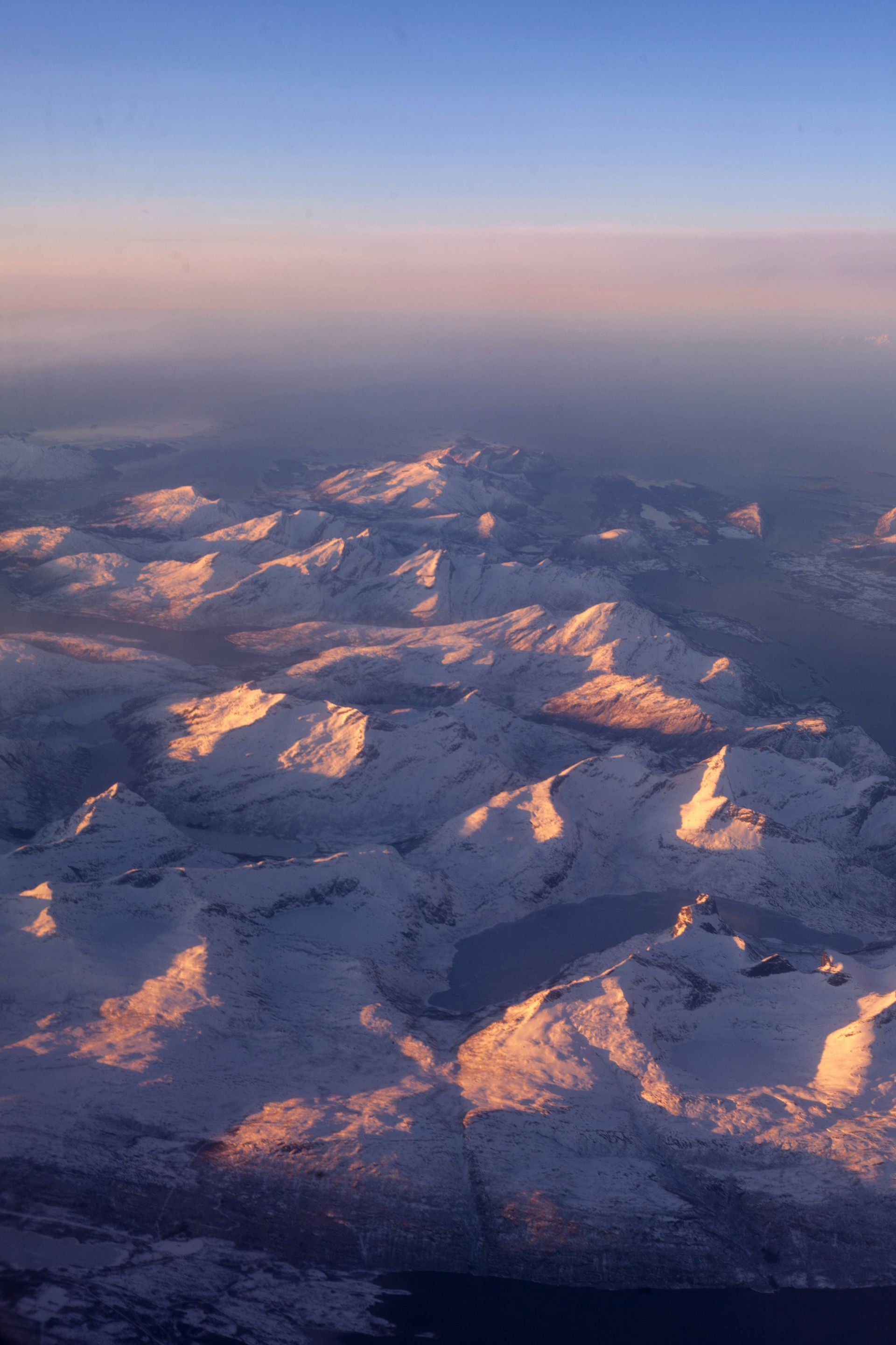 Snow-covered mountains at sunset, viewed from above against a gradient purple sky in Narvik, Norway.