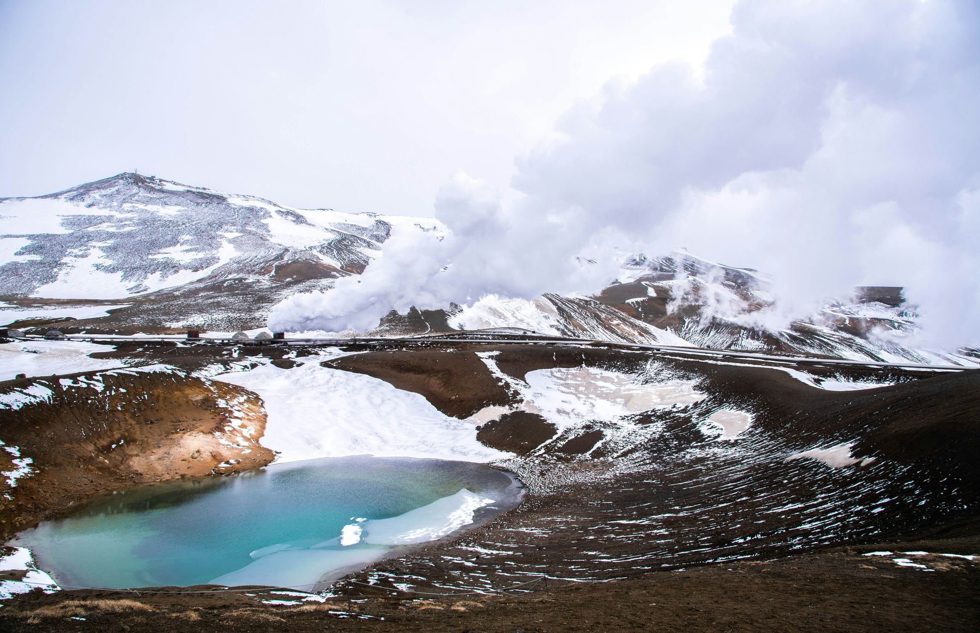 Snowy landscape with a turquoise Askja lake and steam rising from geothermal vents in Iceland.