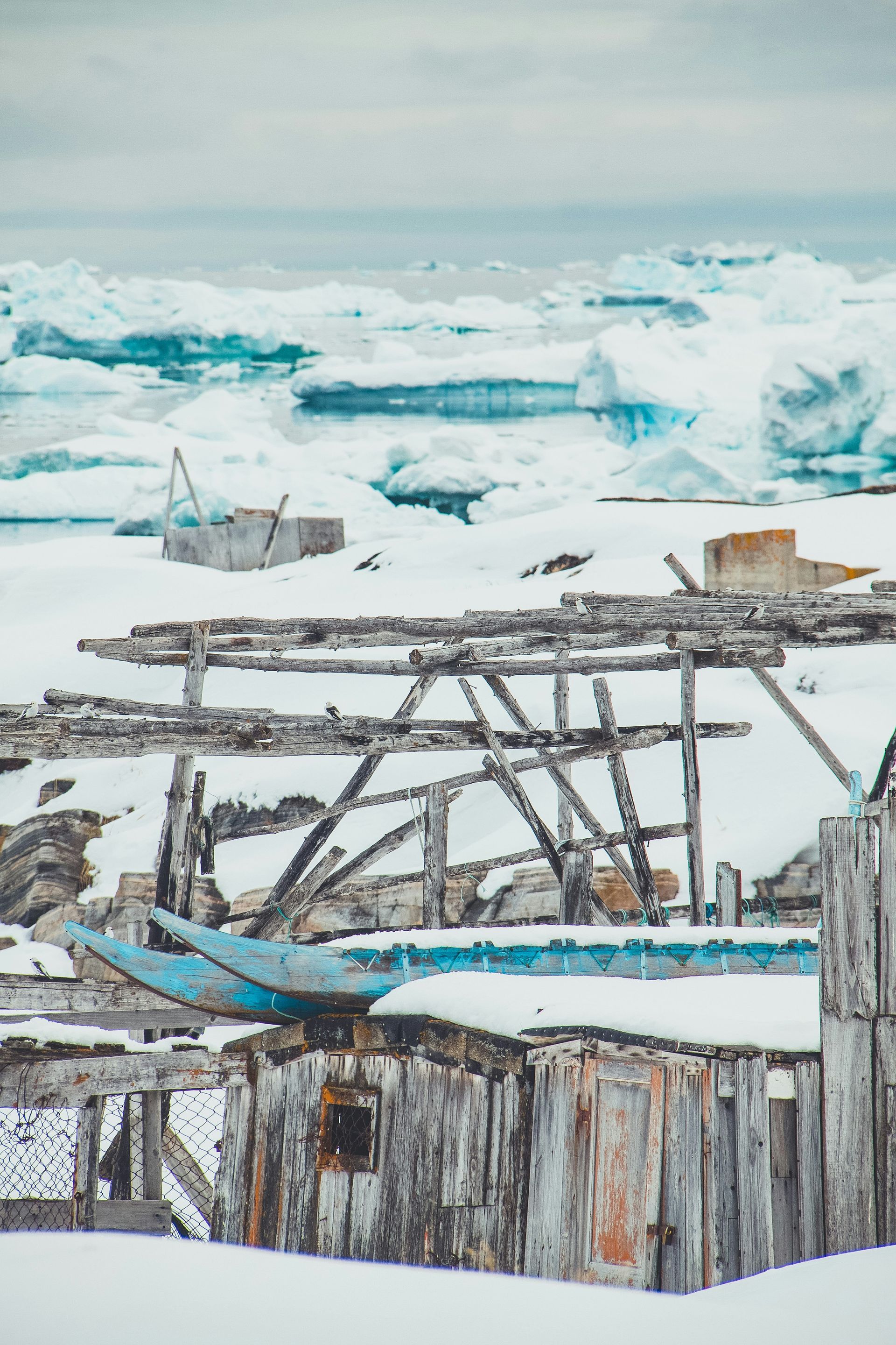 Snowy Arctic scene with wooden structures and icebergs on the water in Disko Bay, Greenland.