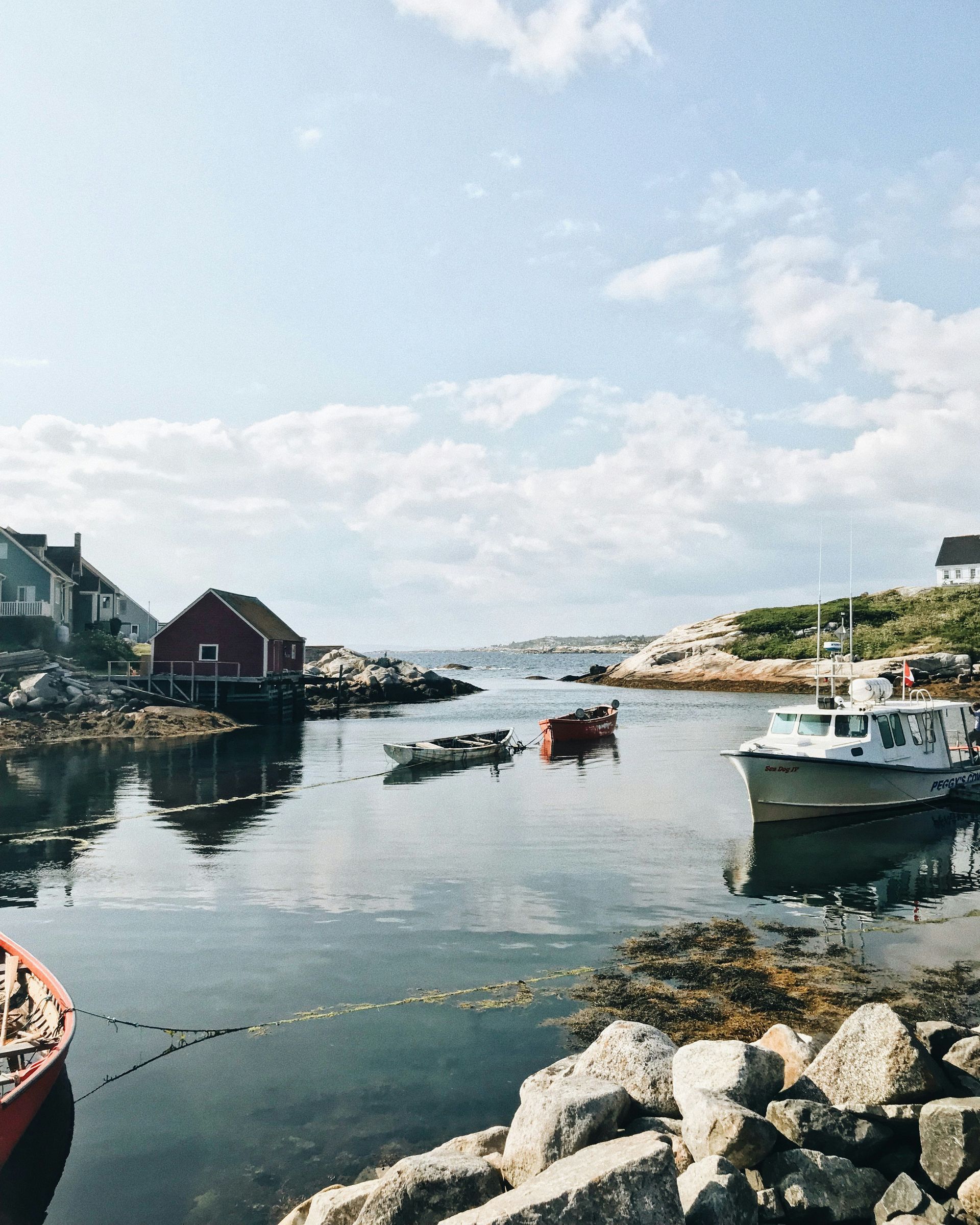Boats in a harbor with a red building, under a partly cloudy sky in Peggy's Cove, Nova Scotia.