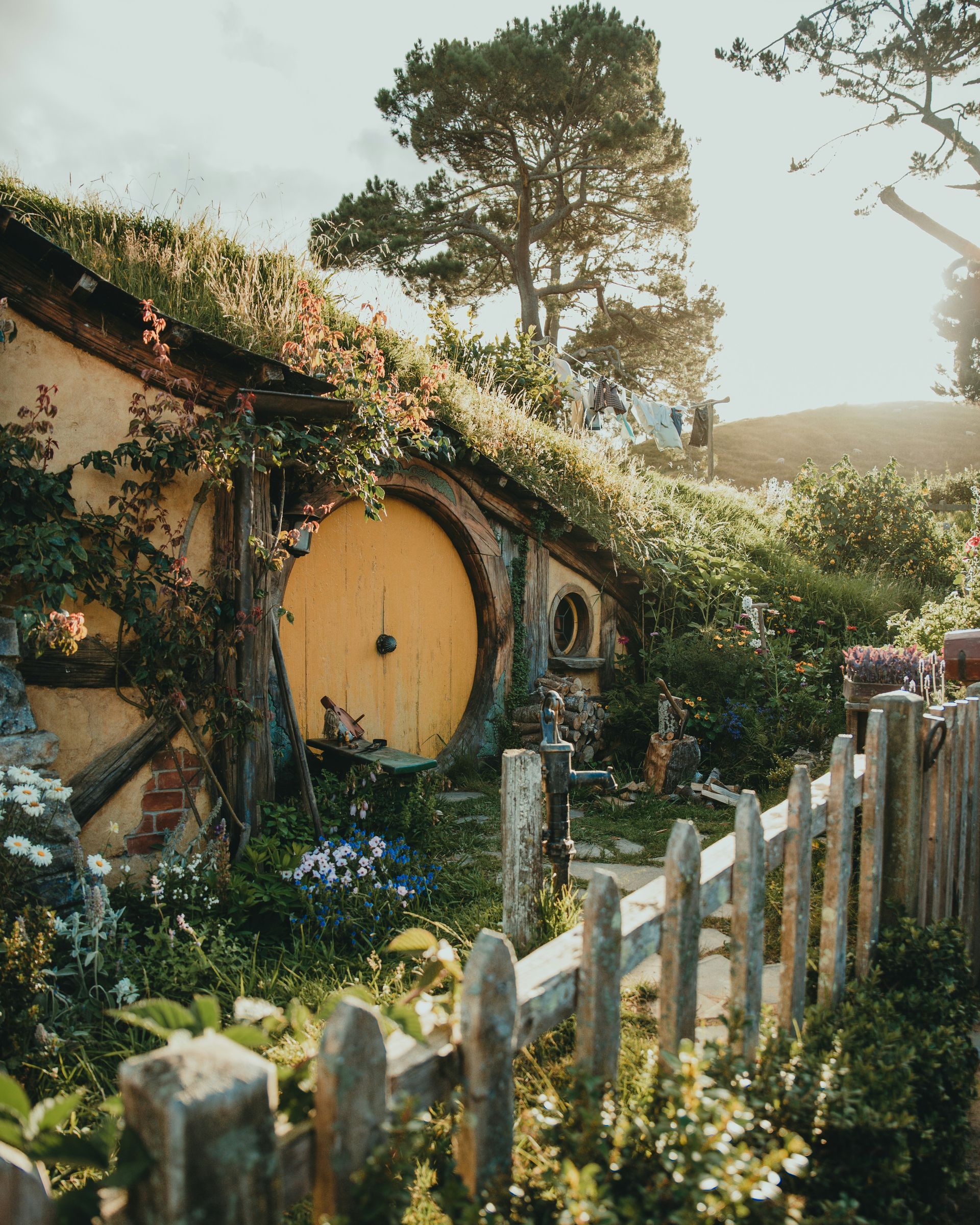 A hobbit house with a yellow door and a wooden fence in front of it at the Hobbiton Movie Set in Matamata, New Zealand.