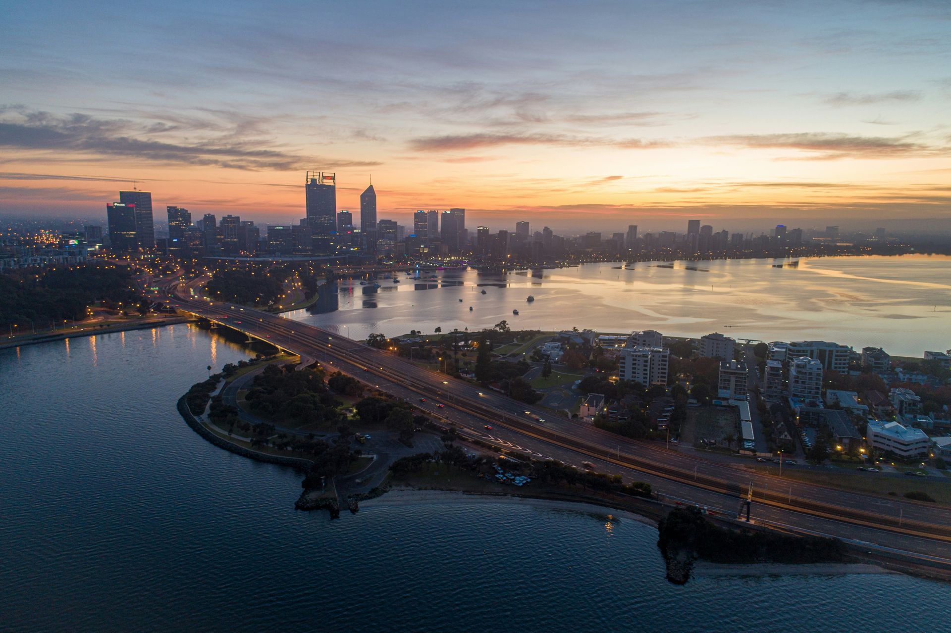 An aerial view of a city with a bridge over a body of water at sunset in Western Australia.