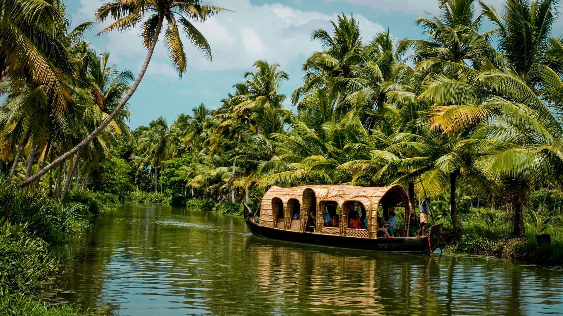 Houseboat on a tranquil river surrounded by lush green palm trees in Kerala, India.