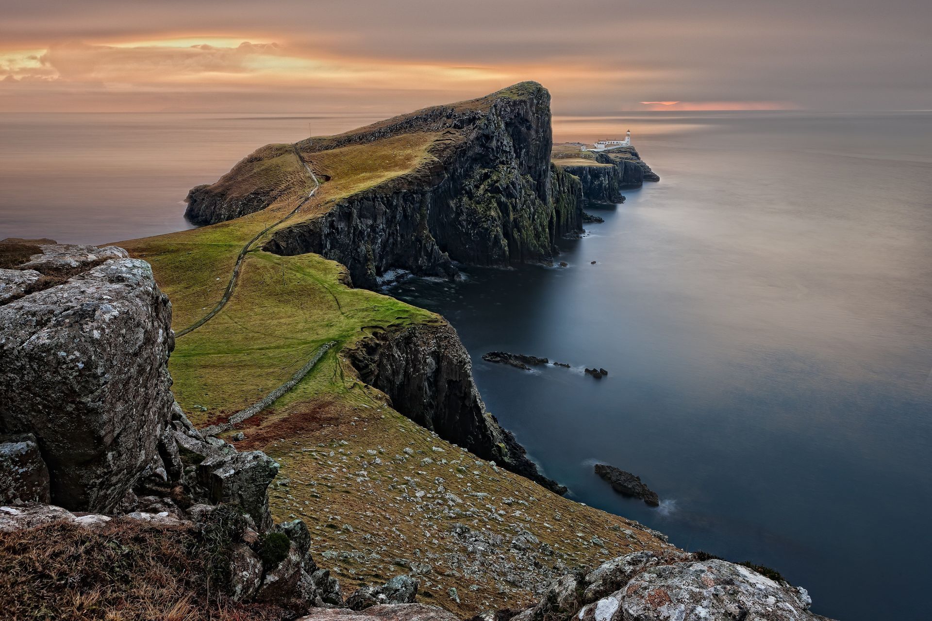 A cliff overlooking the ocean with a sunset in the background in the United Kingdom.