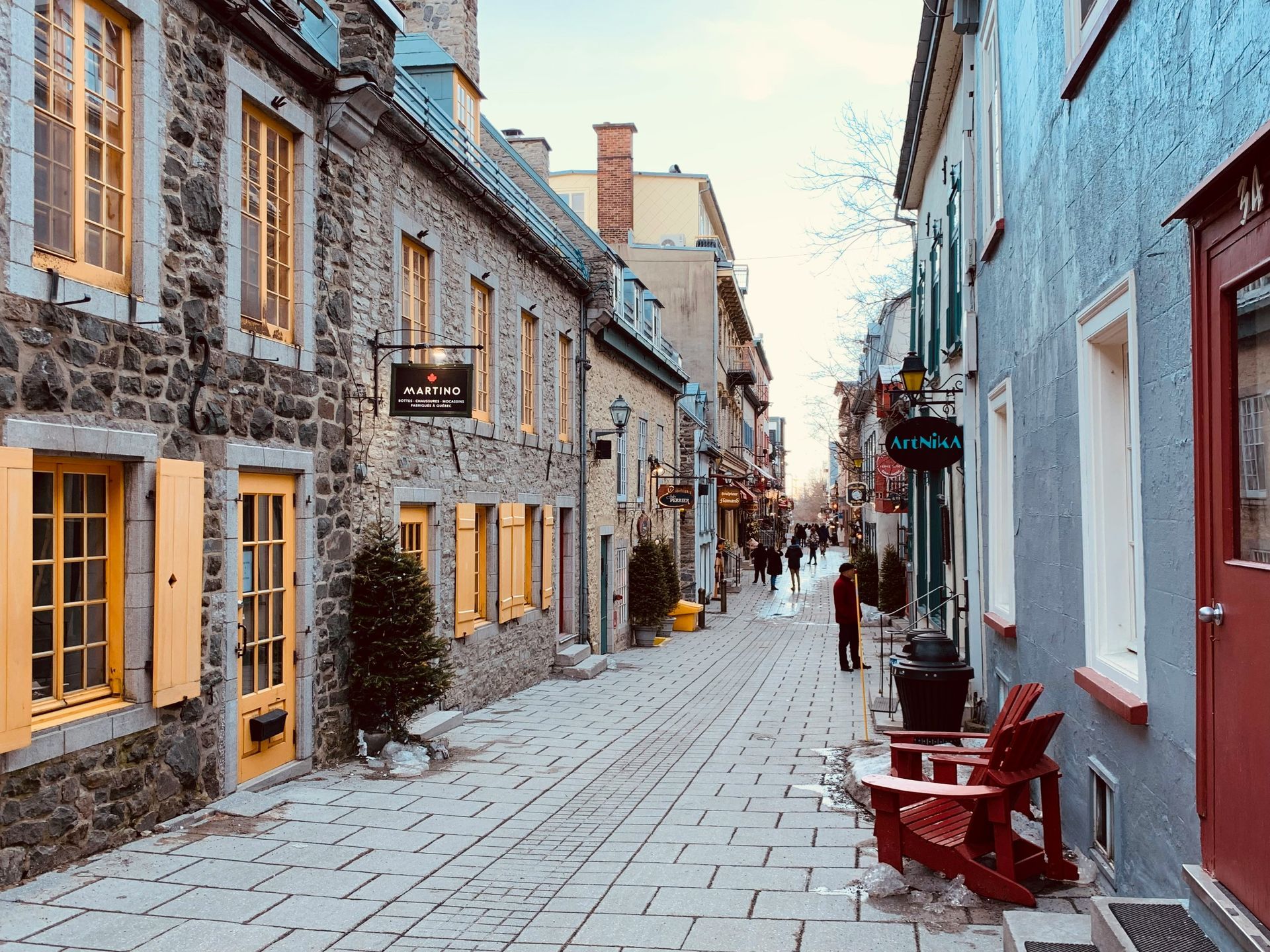 Cobblestone street in Old Quebec, lined with stone buildings featuring colorful doors and shutters. People stroll along the street.