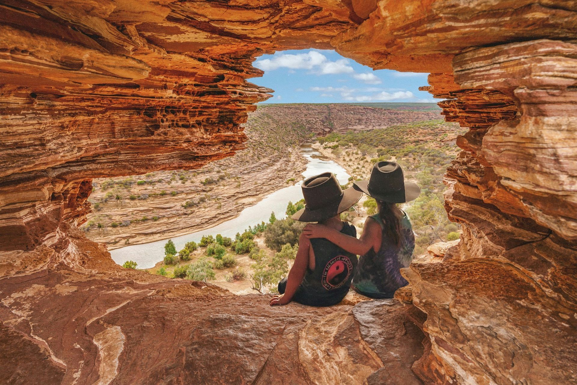 Two people are sitting on a rock looking out of a cave in Western Australia.