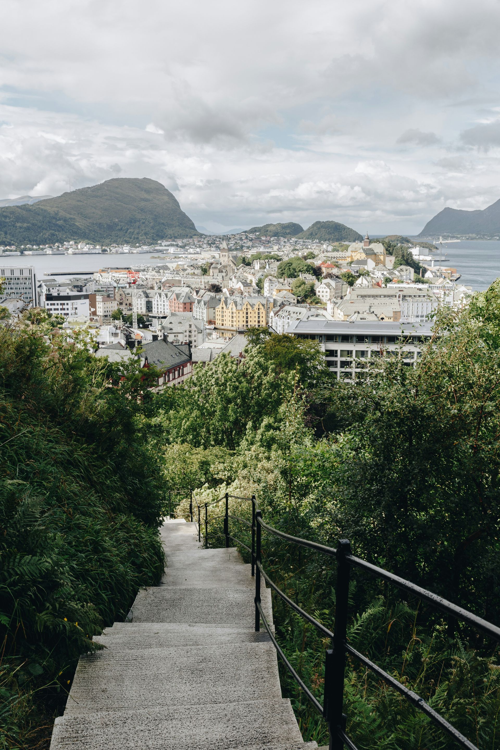 Stone steps descending to a coastal city, surrounded by greenery in Ålesund, Norway.