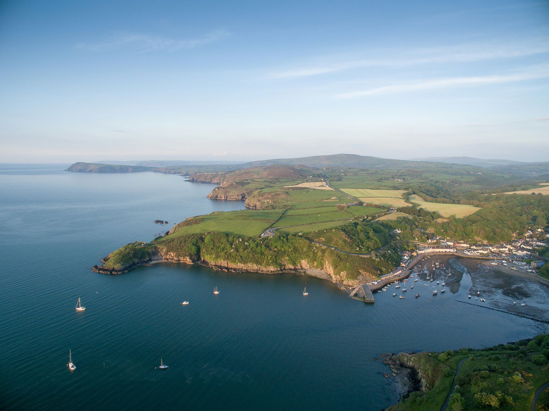 Coastal landscape with boats in the water and green cliffs under a blue sky in Pembrokeshire, Wales.