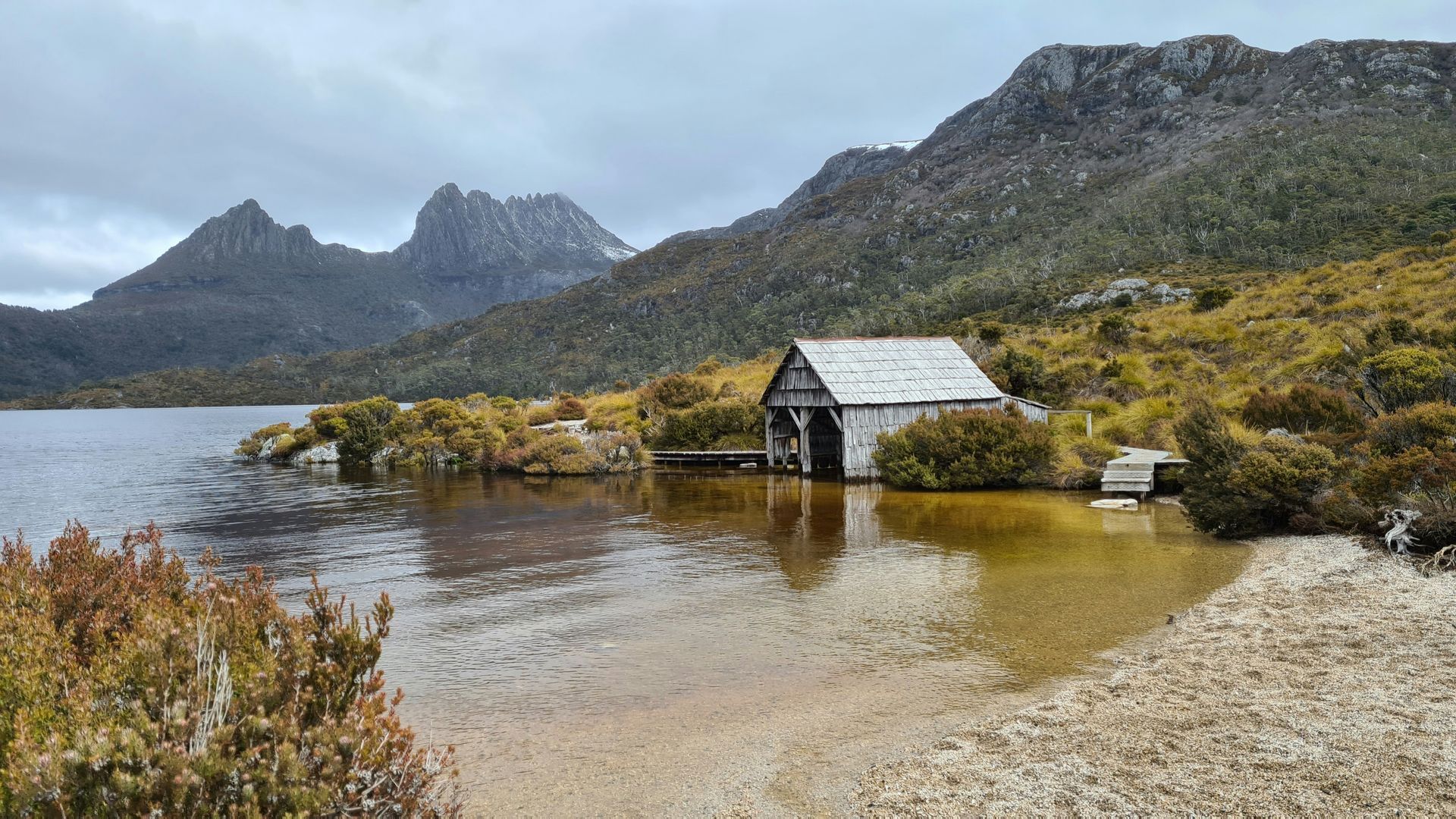 A small house is sitting in the middle of a lake with mountains in the background in Tasmania, Australia.