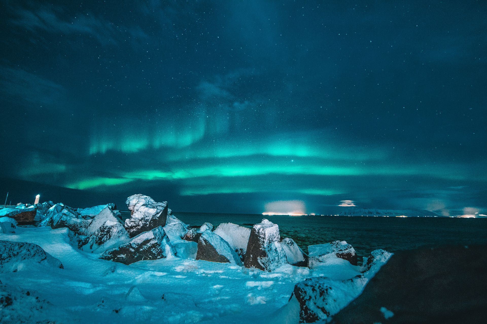 Northern Lights over a snowy shoreline, with green and teal aurora borealis, and a starry sky in Iceland.