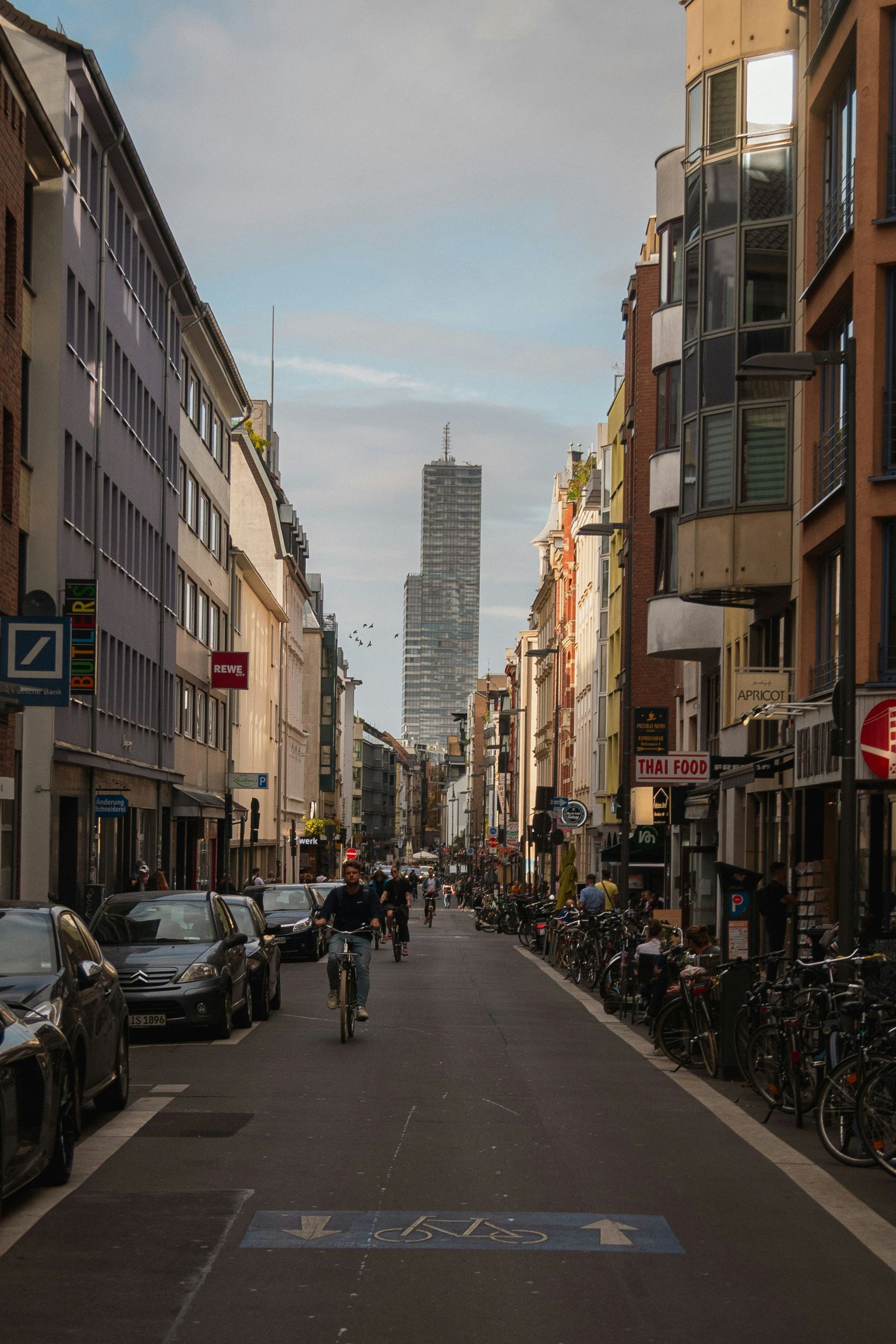 Street view of a city with tall buildings and a skyscraper in the distance in Cologne, Germany.