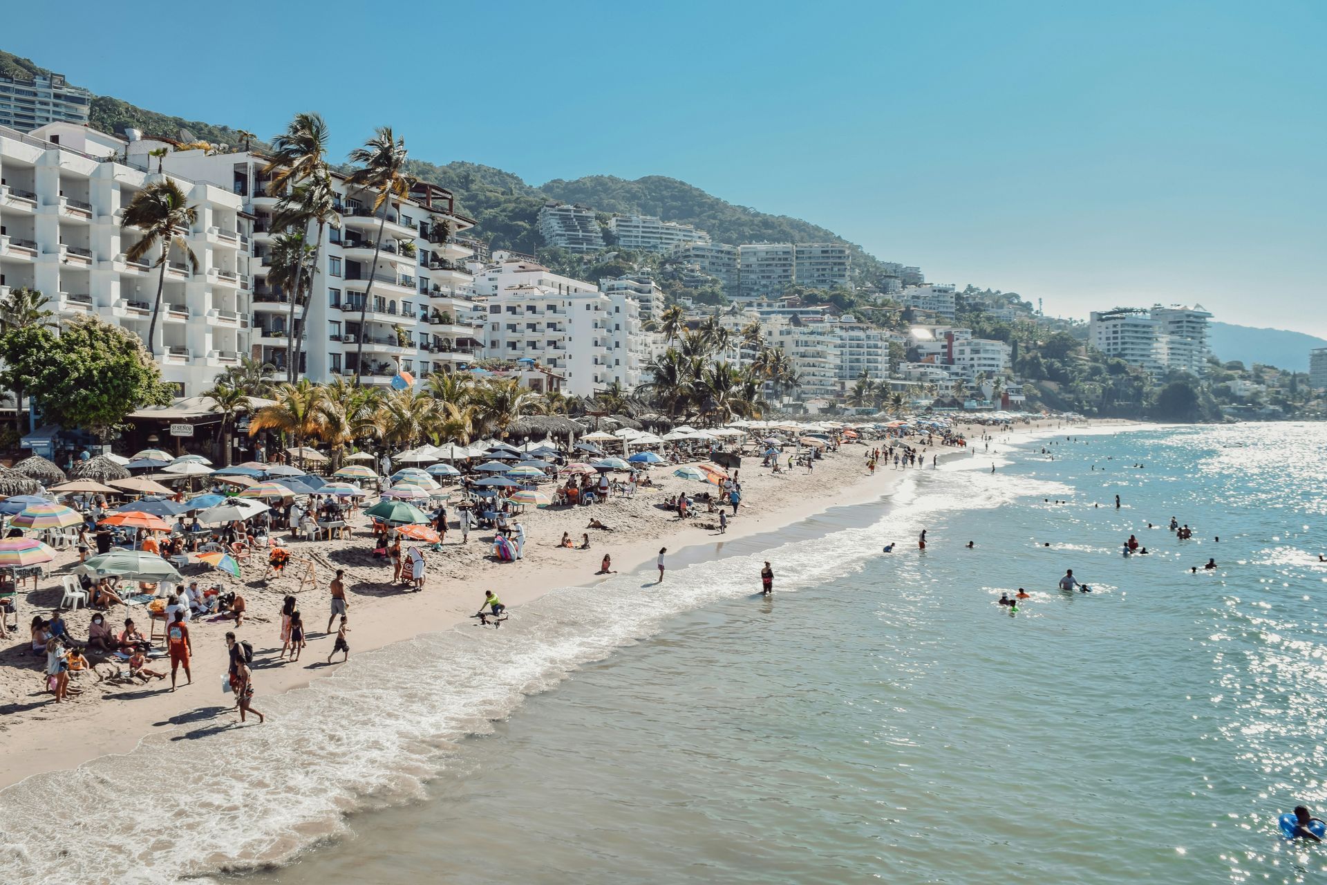 Beach scene in Puerto Vallarta, Mexico, with white buildings and green hills in the background.