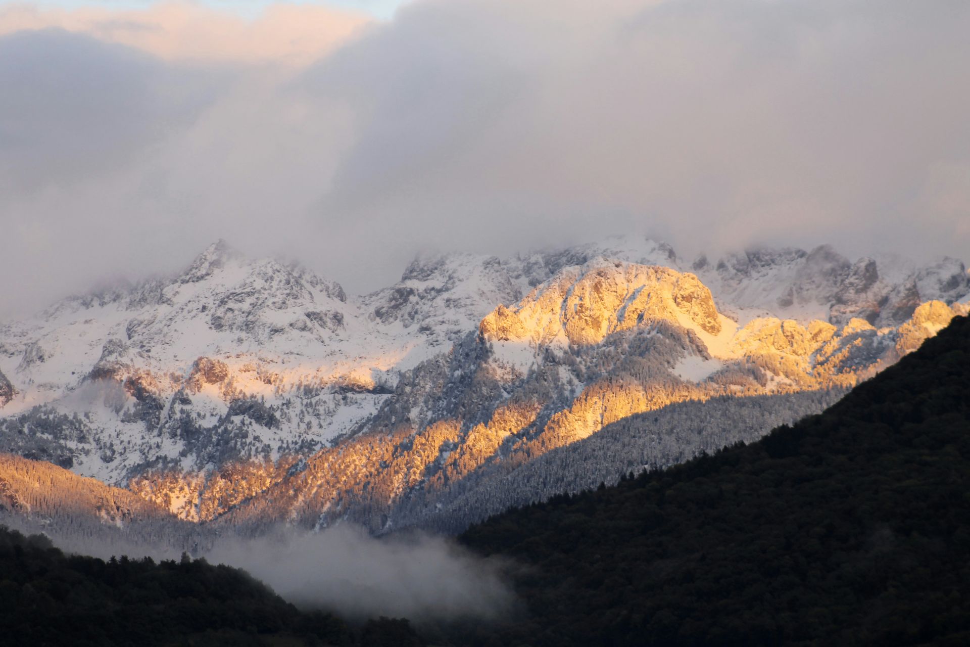 A snowy mountain range with the sun shining through the clouds in Grenoble, France.