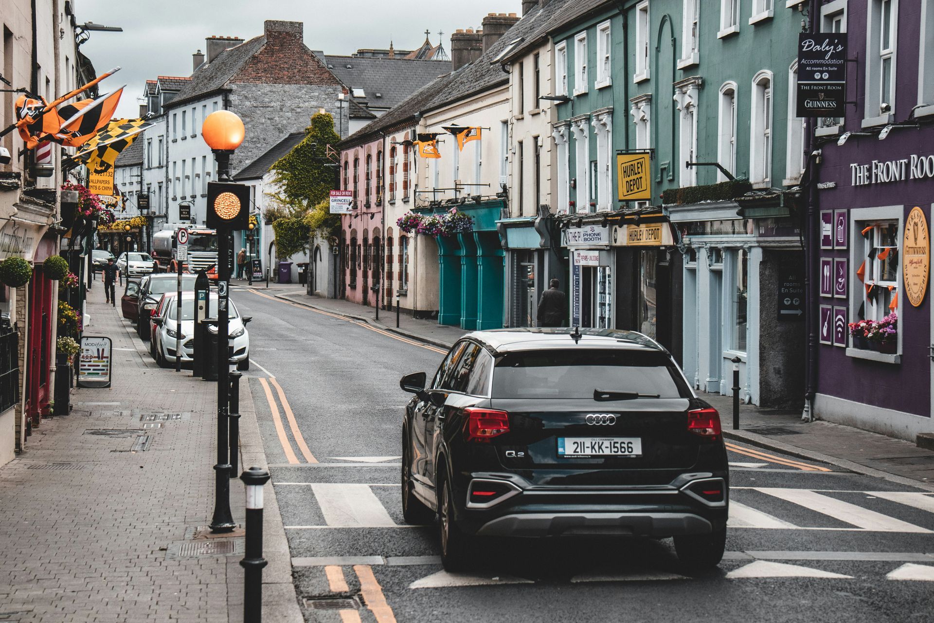Black car at a crosswalk on a narrow street lined with colorful shops and buildings in Kilkenny, Ireland.
