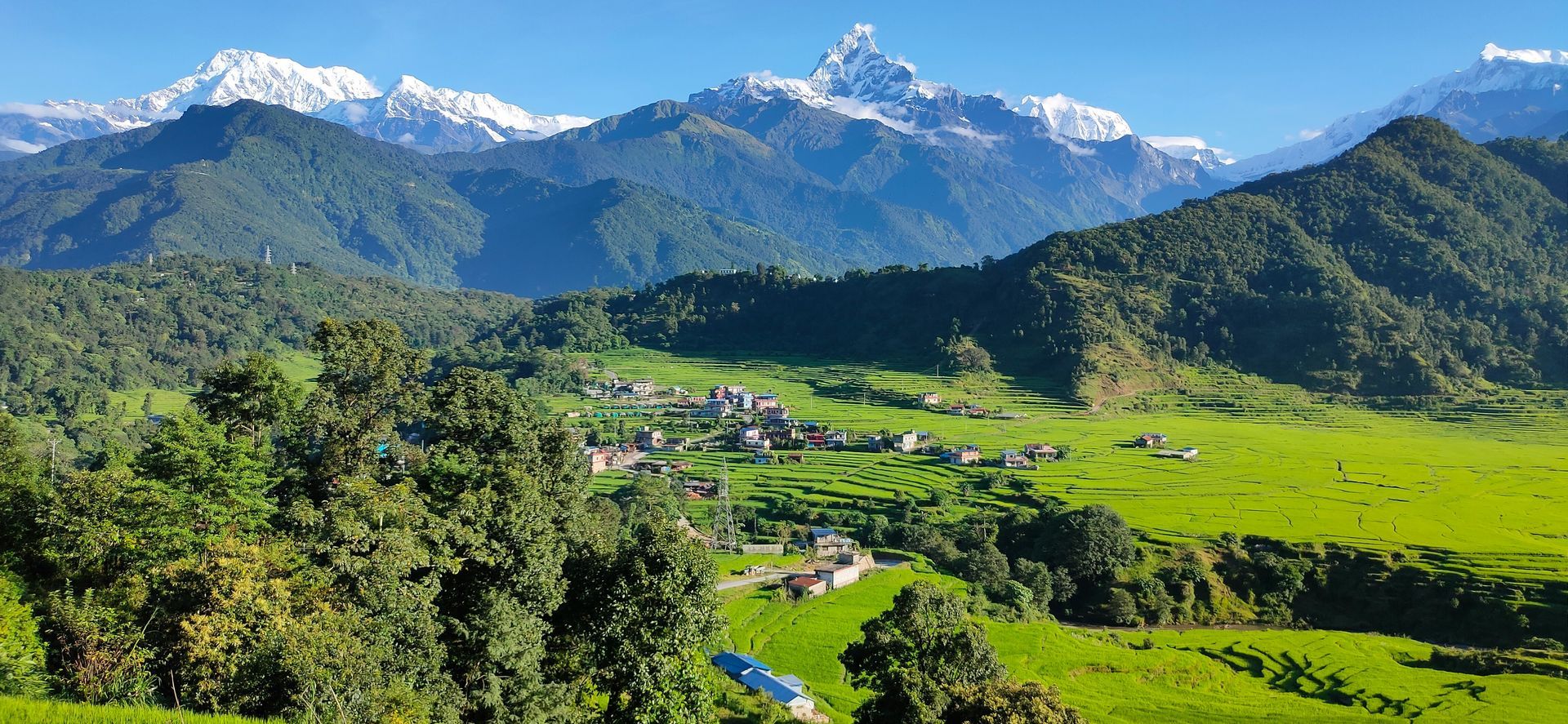 Green valley with a village and snow-capped mountains in Pokhara, Nepal.